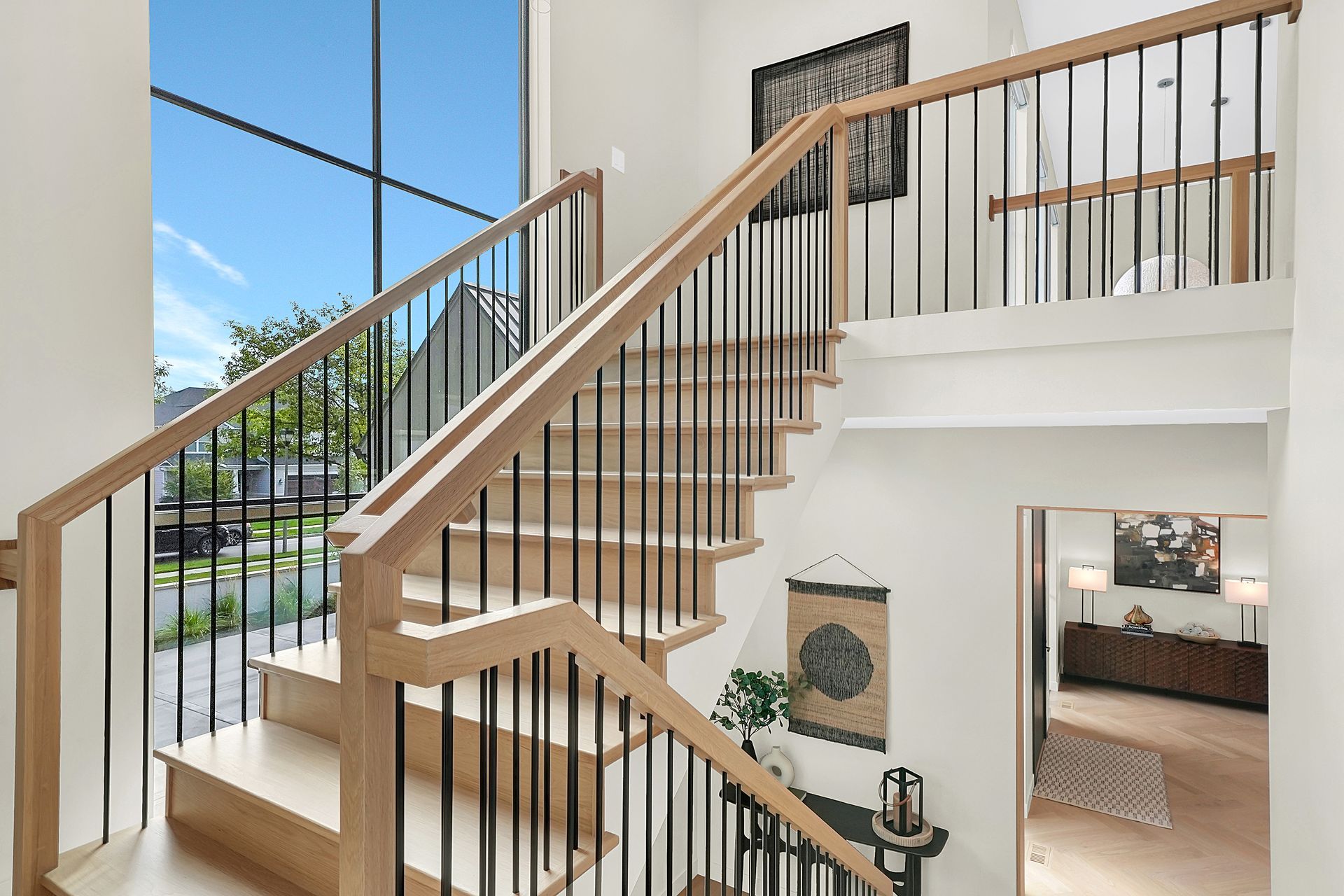 Bright foyer with modern wooden staircase, black railing, and open views to a sunlit home interior