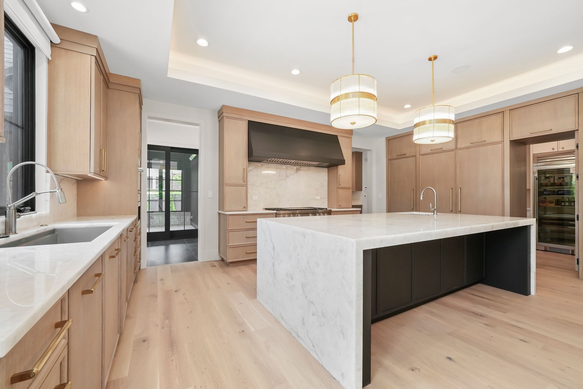 Bright modern kitchen with white island, light wood cabinets, stainless appliances, and pendant lights