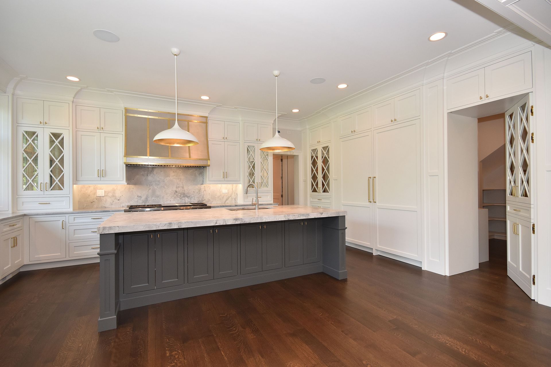 Bright modern kitchen with white cabinets, dark island, marble counters, and hardwood floors
