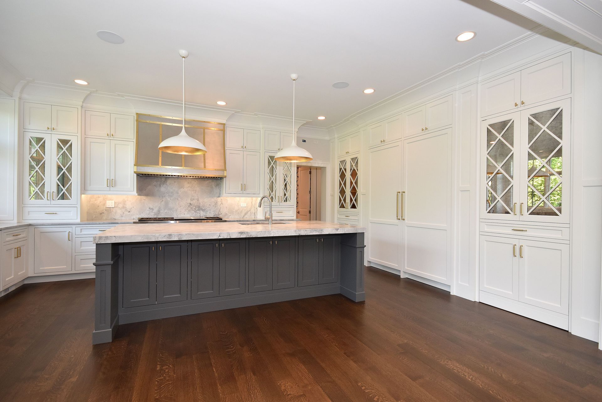 Bright white kitchen with a dark island, marble counters, and warm wood floors