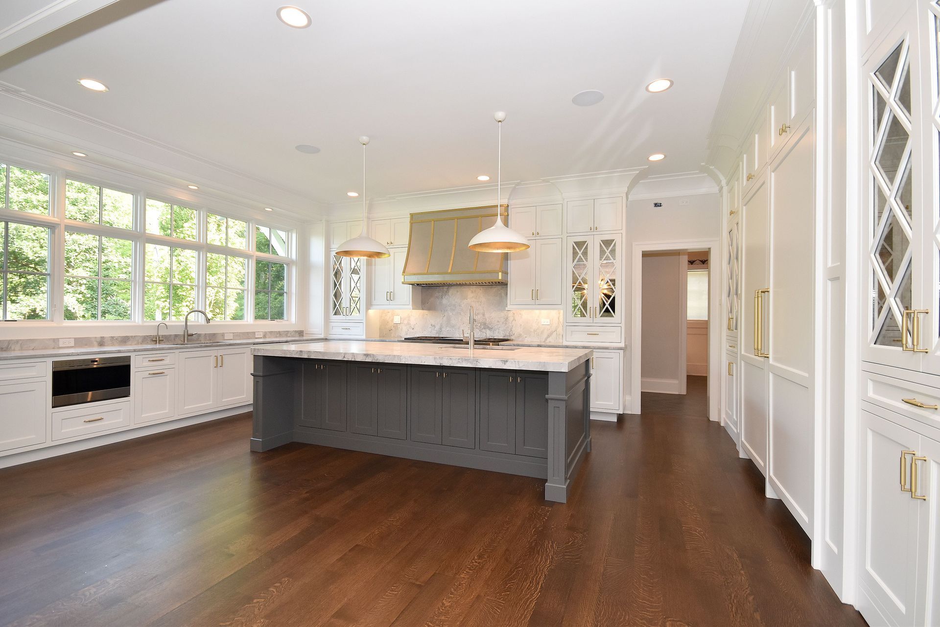 Bright white kitchen with dark hardwood floors, large island, and stainless steel range hood