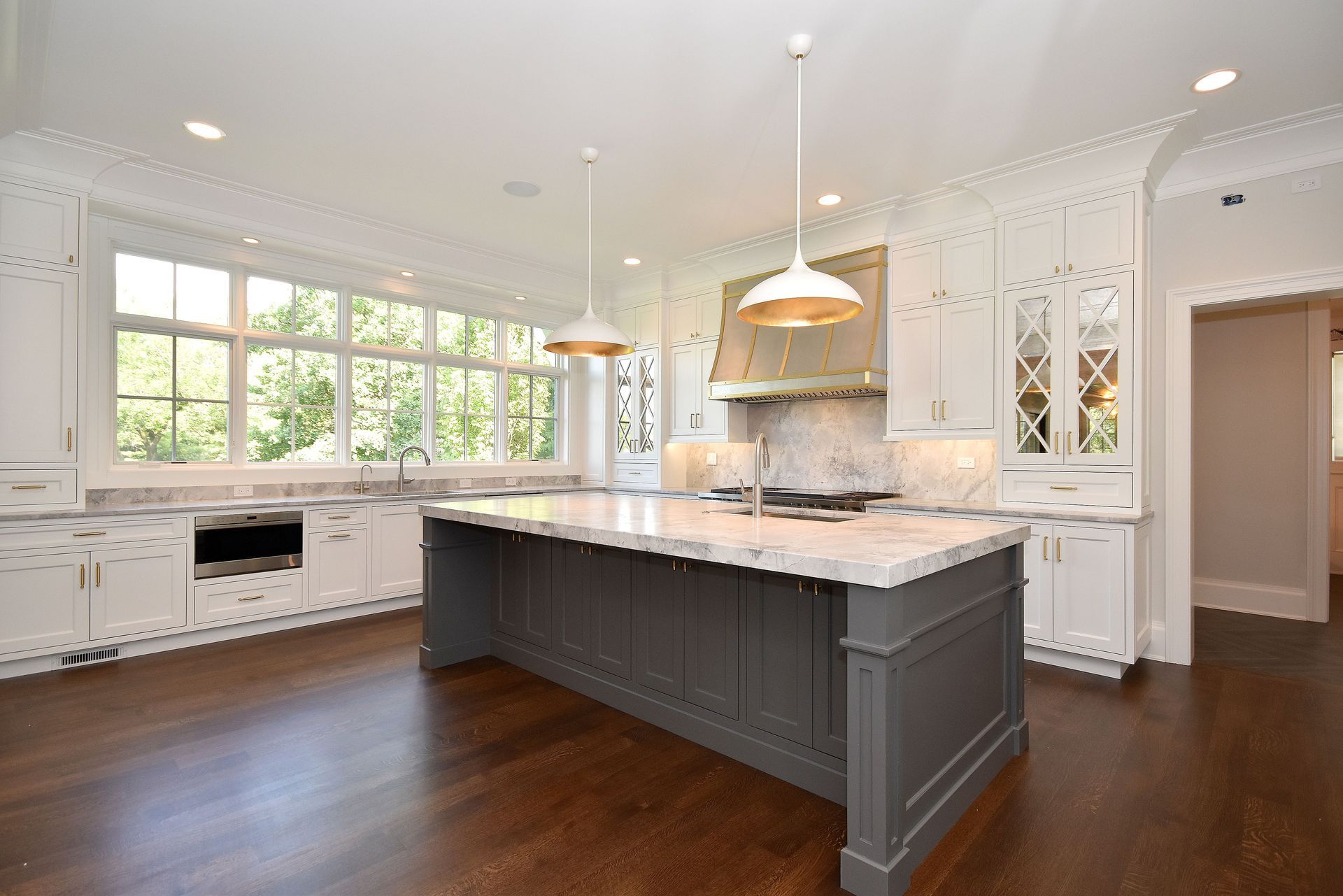 Bright white kitchen with dark island, hardwood floors, and large windows