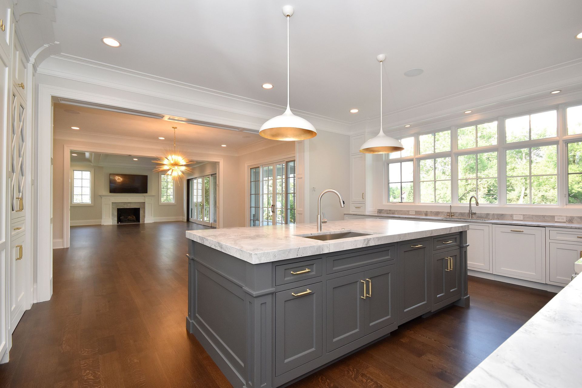 Bright modern kitchen with a gray island, white cabinets, pendant lights, and hardwood floors
