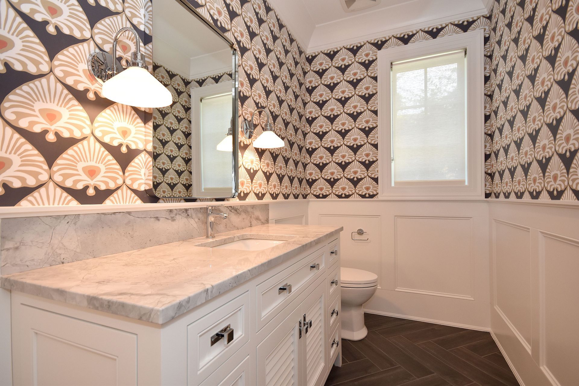 Bright bathroom with floral wallpaper, white vanity, marble countertop, and a toilet near a window.