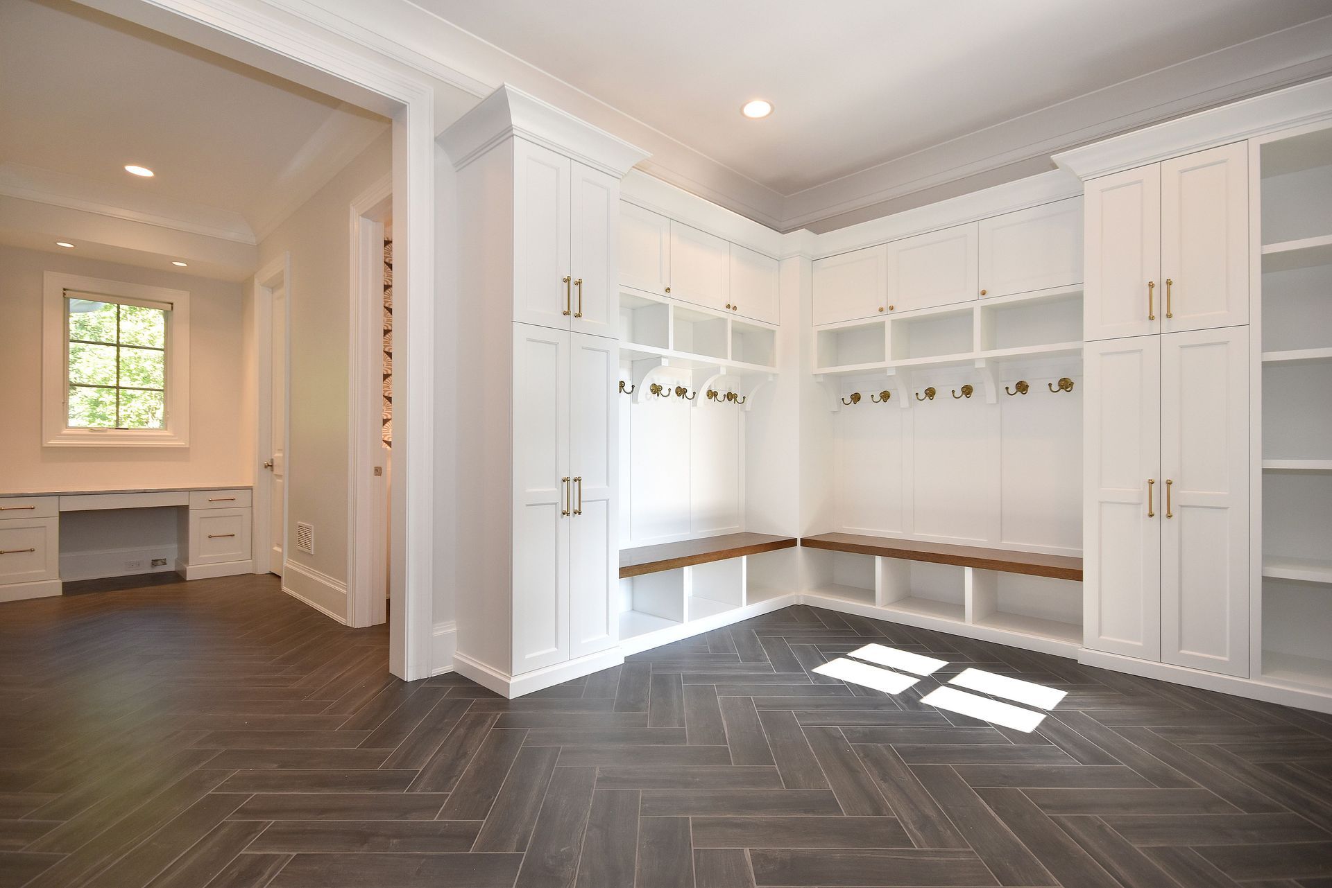 Bright white walk-in closet with built-in shelving, bench seating, and dark herringbone wood floor.