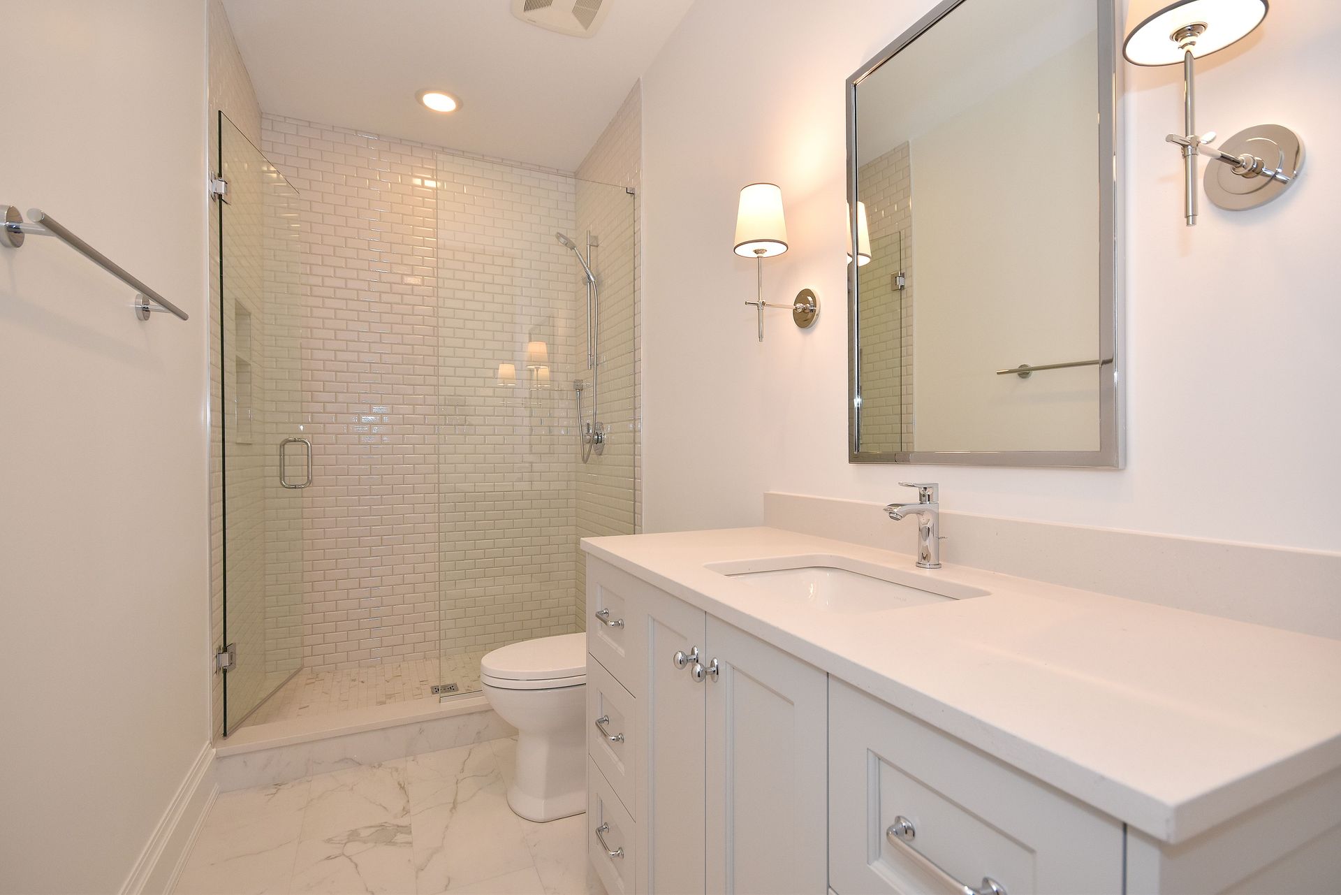 Bright modern bathroom with white vanity, large mirror, glass shower, and tiled walls