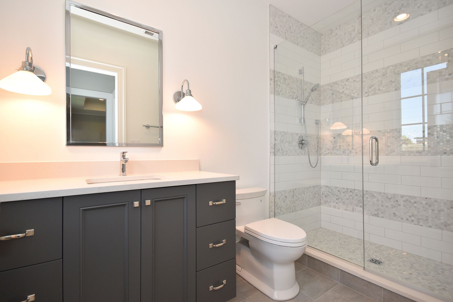 Modern bathroom with dark vanity, large mirror, toilet, and glass-enclosed shower