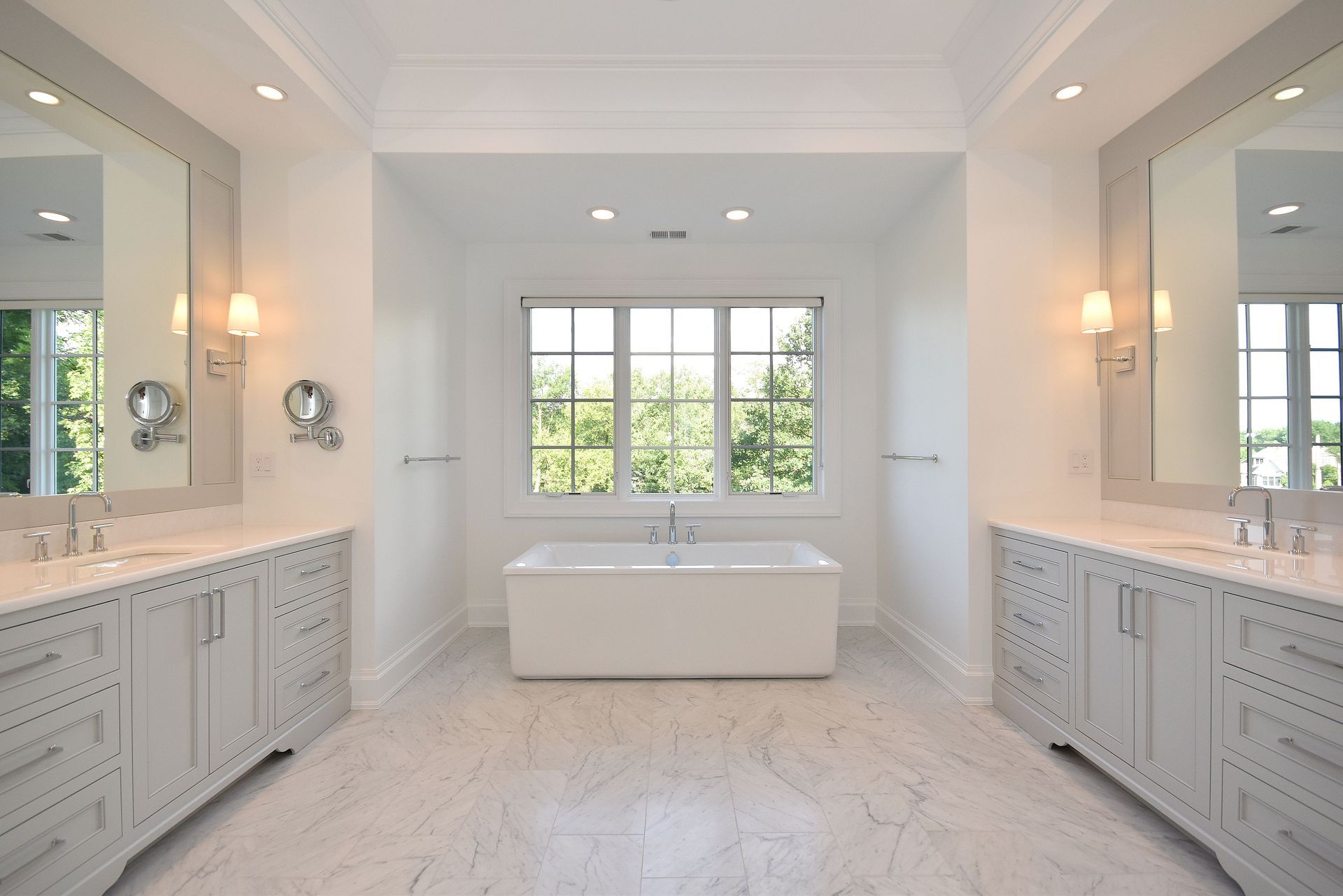 Bright white spa bathroom with double vanities, large mirrors, soaking tub, and window view.