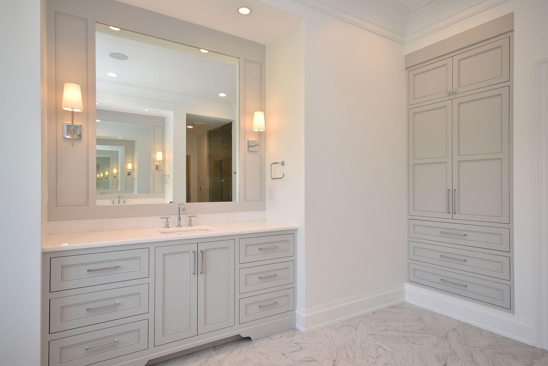 Bright white bathroom vanity with large mirror, wall sconces, and built-in cabinets in a tiled room