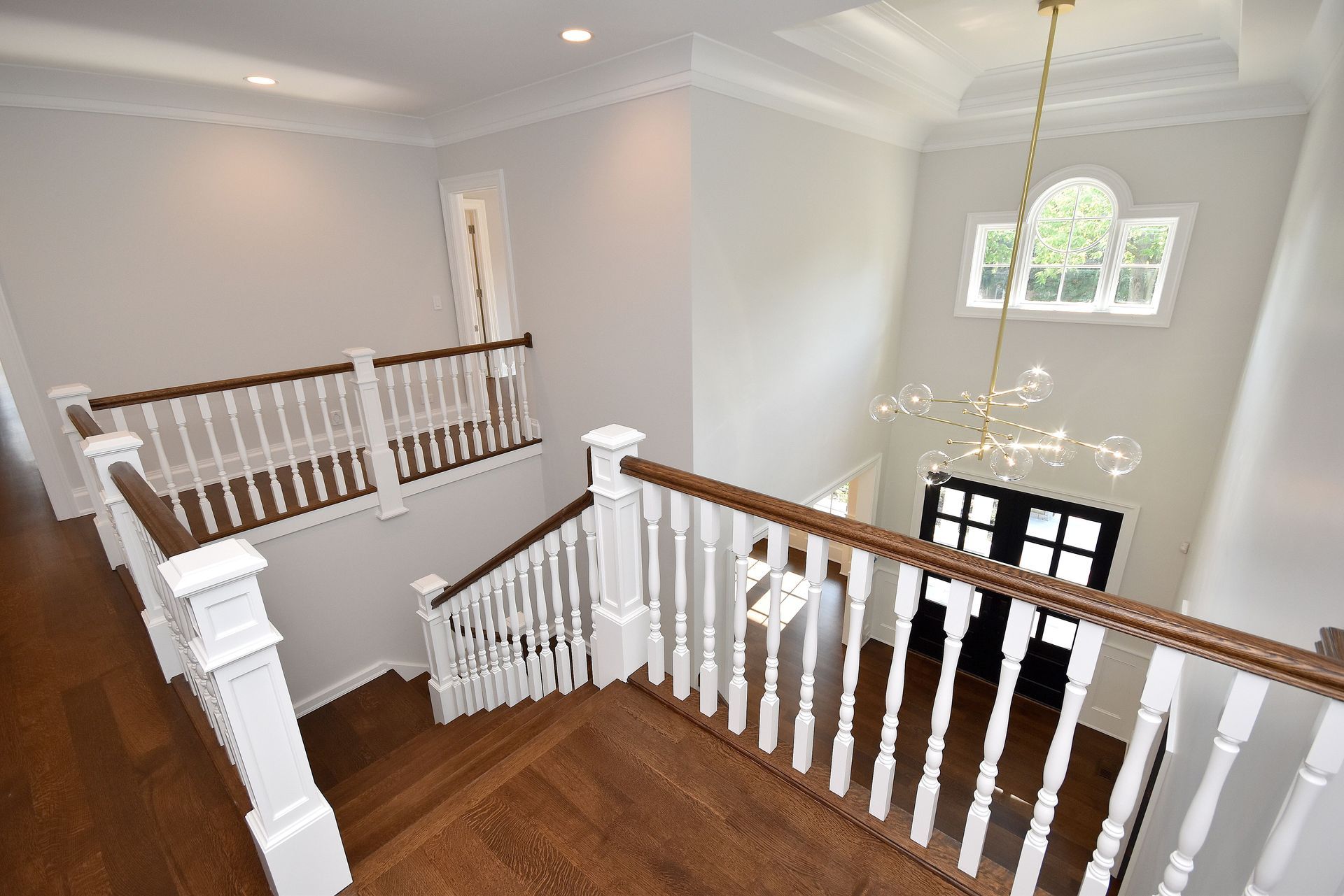 Bright upstairs landing with white railings, wood floor, and a window overlooking the foyer below