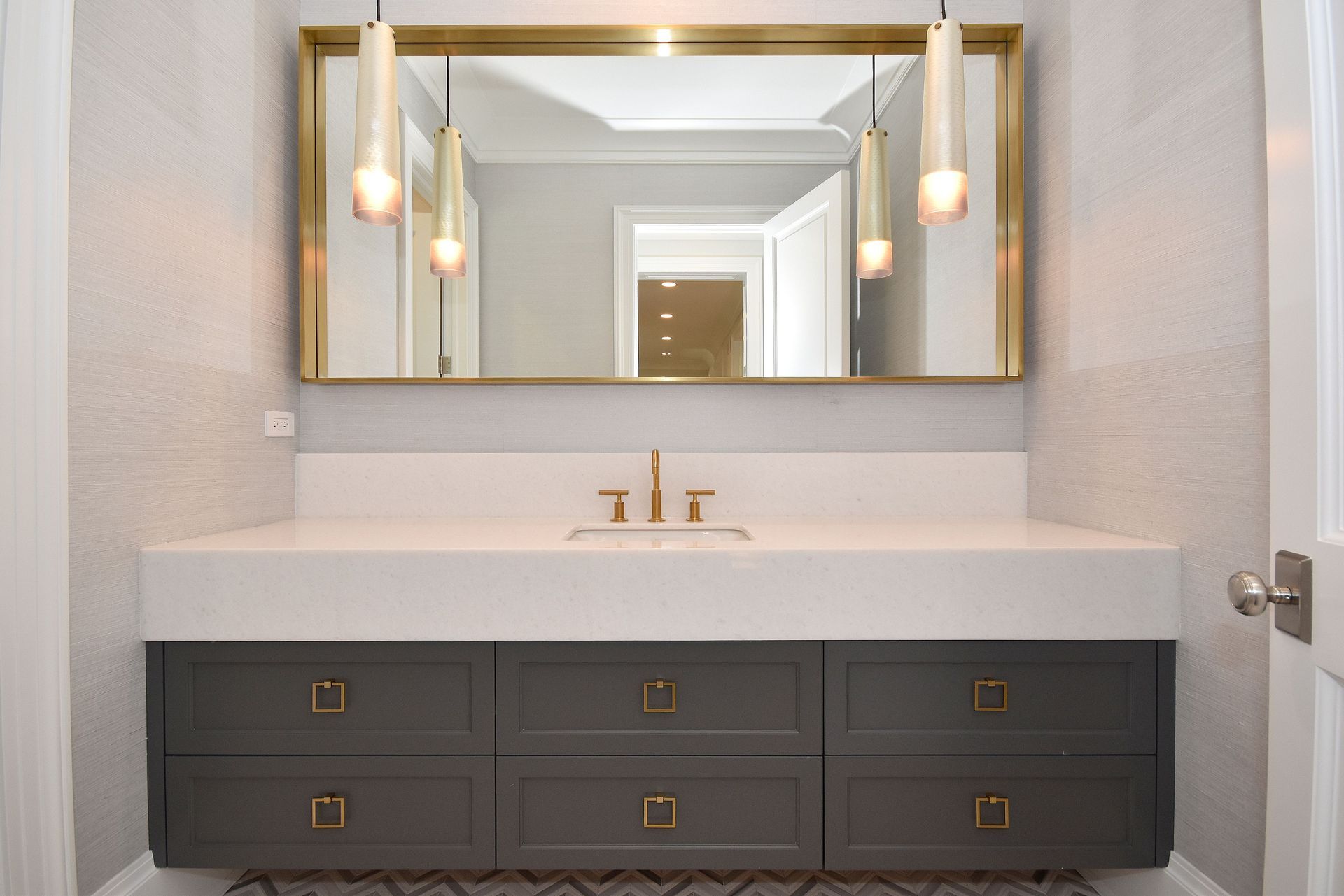 Modern bathroom vanity with dark drawers, white countertop, gold-framed mirror, and wall sconces