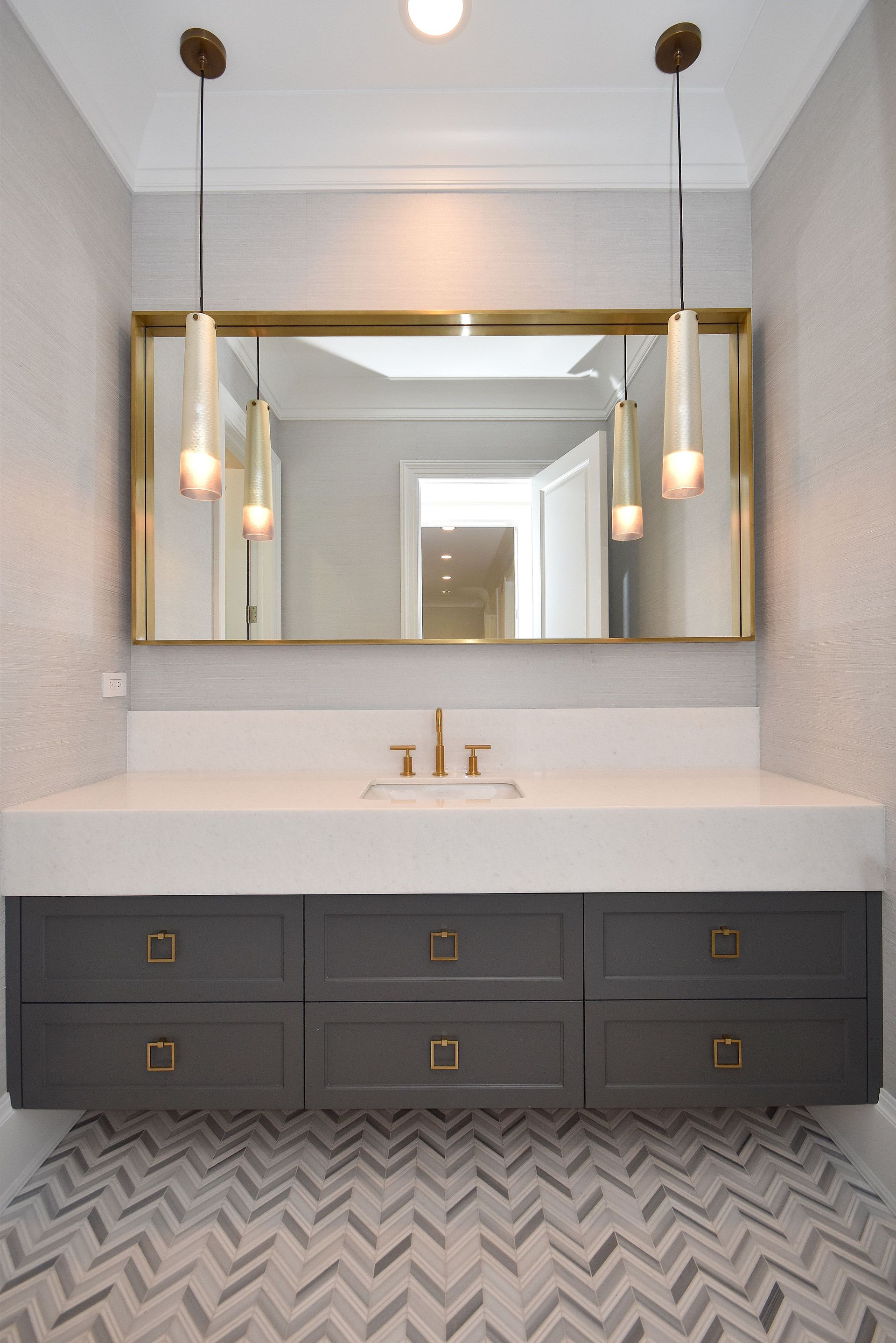 Modern bathroom vanity with black drawers, white countertop, large mirror, and pendant lights over patterned floor tile