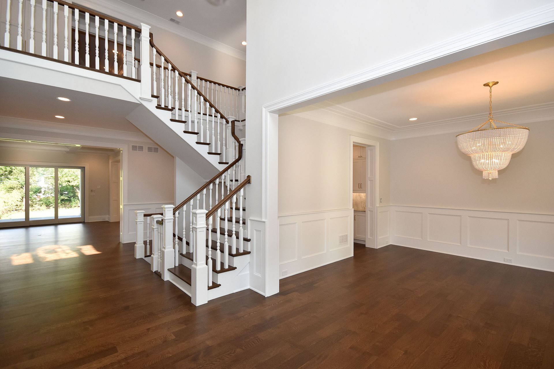 Bright foyer and dining room with hardwood floors, white trim, staircase, and chandelier
