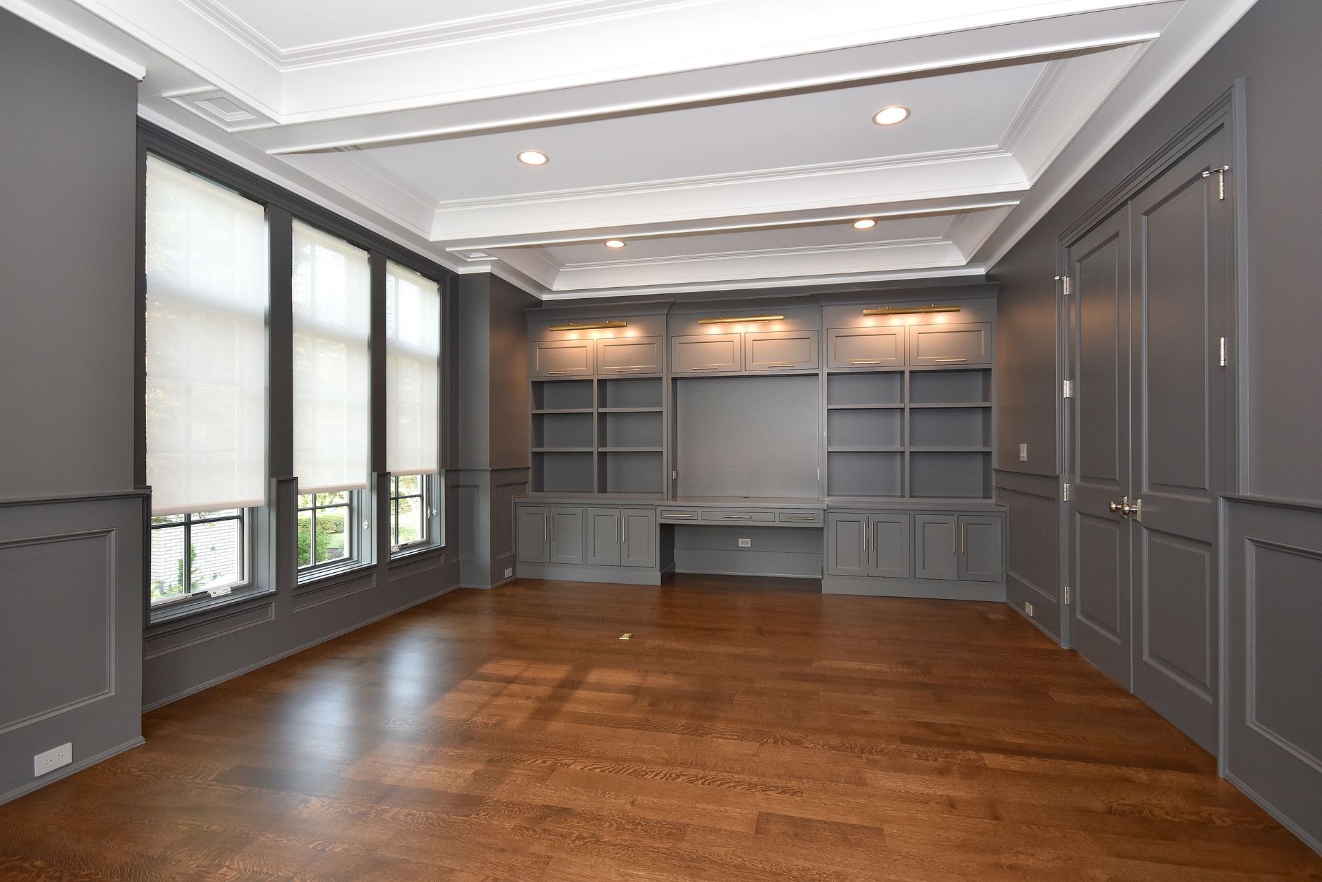 Empty modern room with gray built-in cabinetry, hardwood floor, and large windows