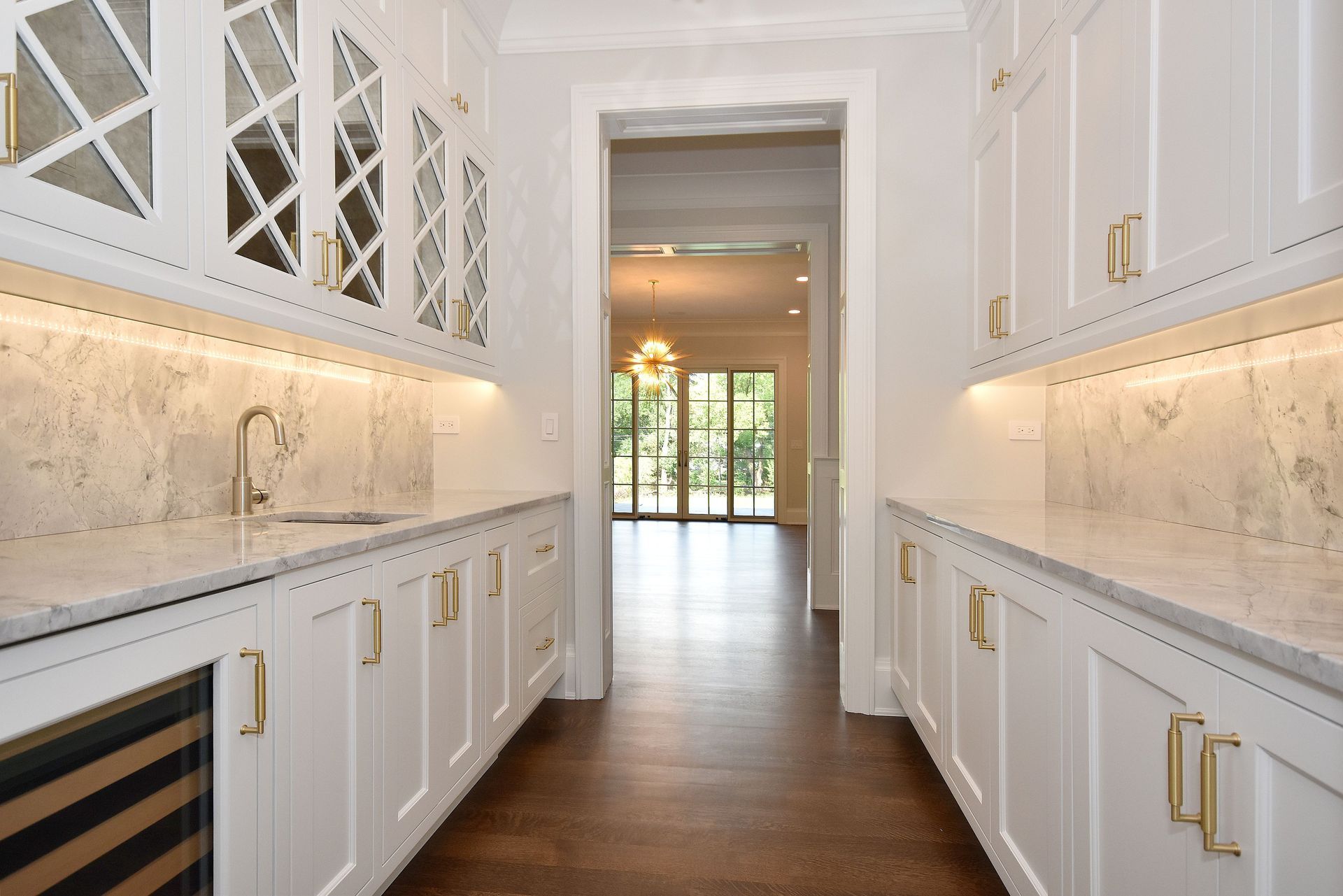 Bright white galley kitchen with marble counters, gold accents, and wood floors leading to a glass door