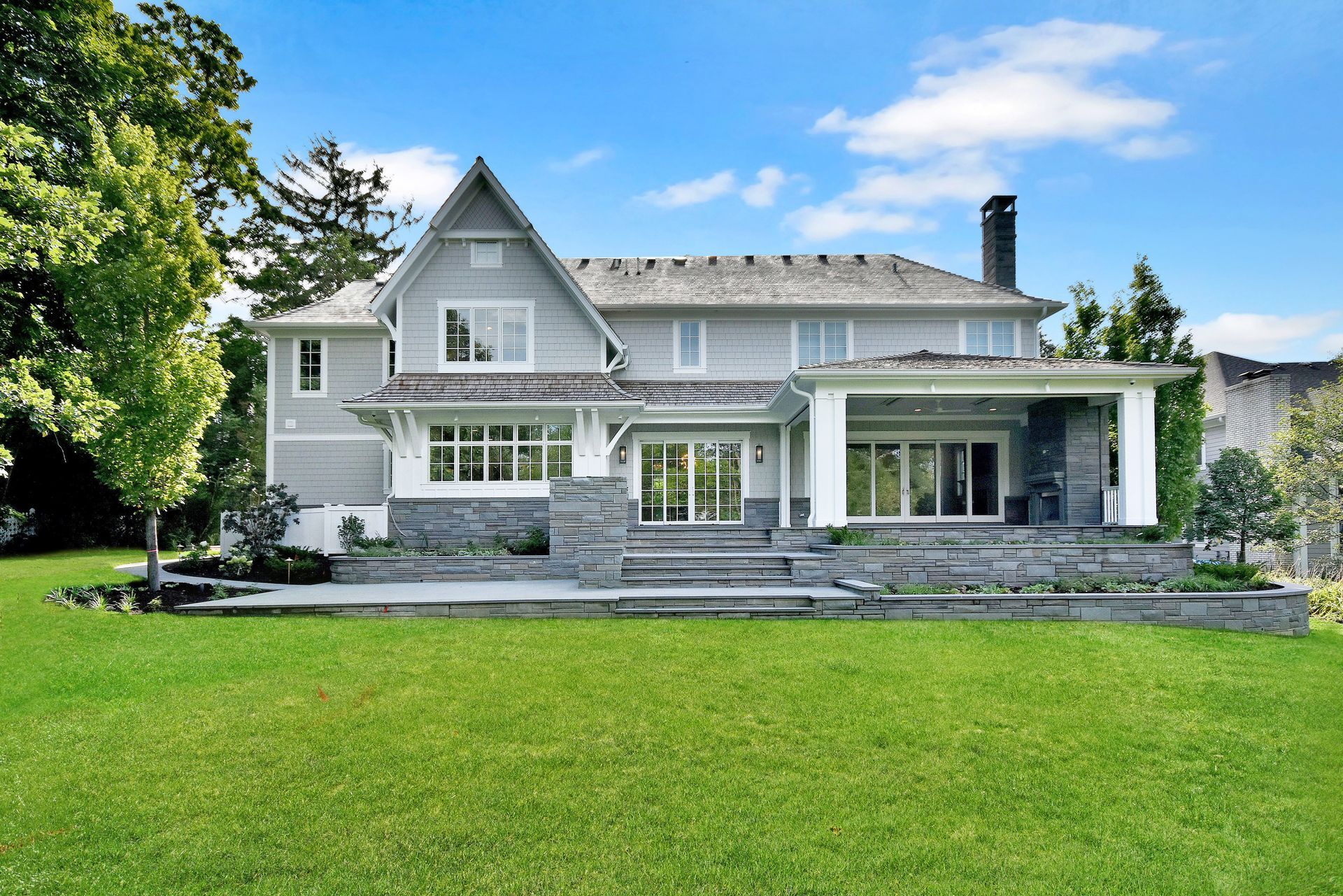 Large white house with a gray roof, front porch, and expansive green lawn under a blue sky