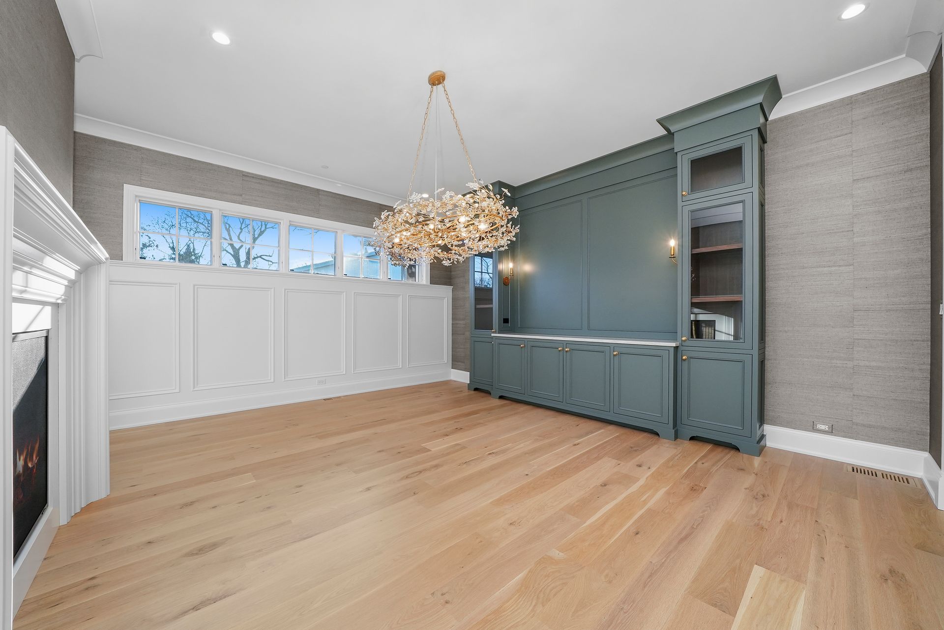 Empty dining room with light wood floors, blue built-in cabinets, and a modern chandelier.