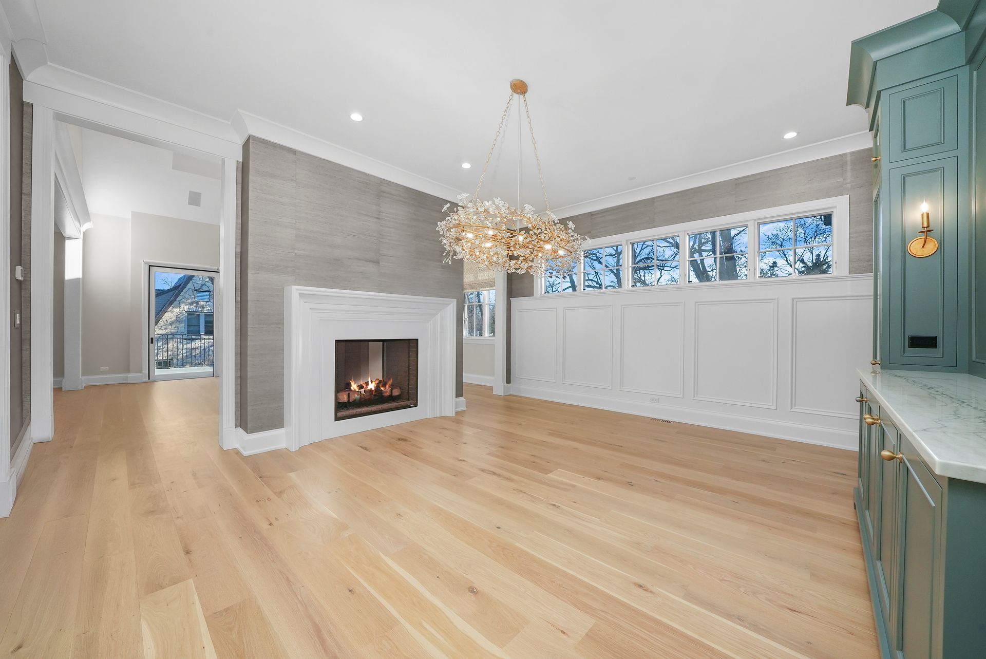 Bright living room with hardwood floors, fireplace, chandelier, and large windows with white wainscoting