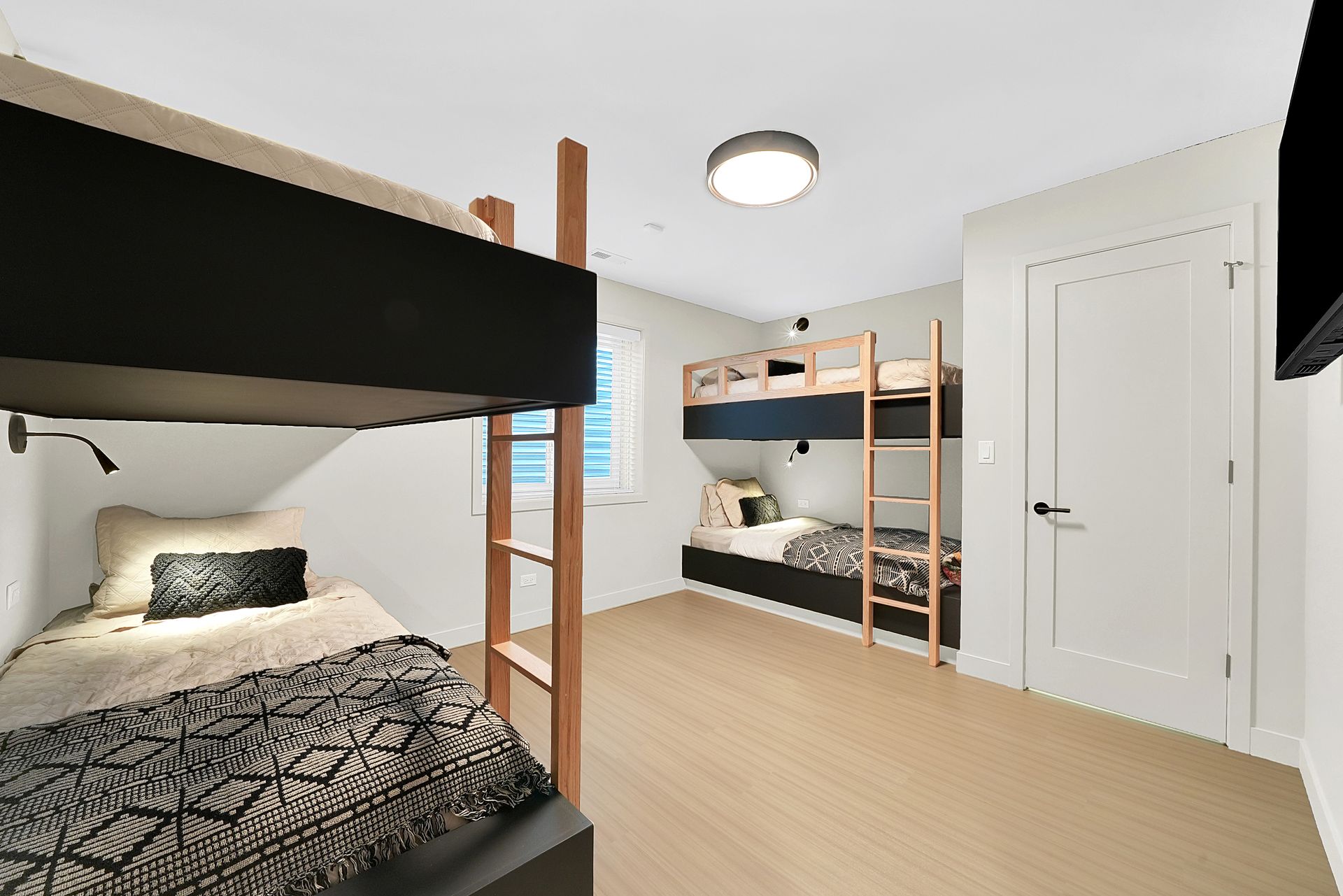 Shared bedroom with two black bunk beds, white walls, light wood floor, and a central ceiling light.