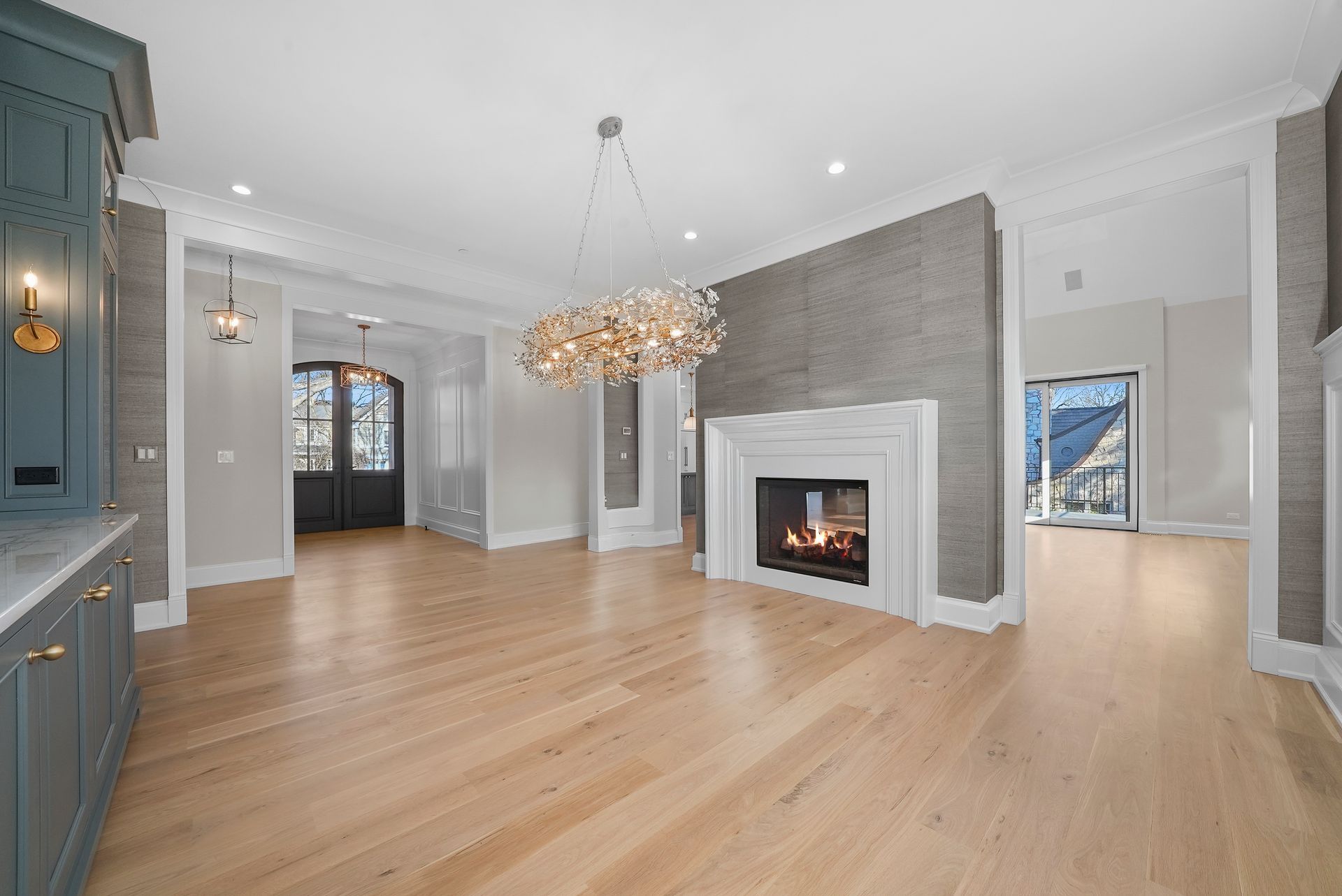 Bright empty living room with hardwood floors, fireplace, chandelier, and gray walls