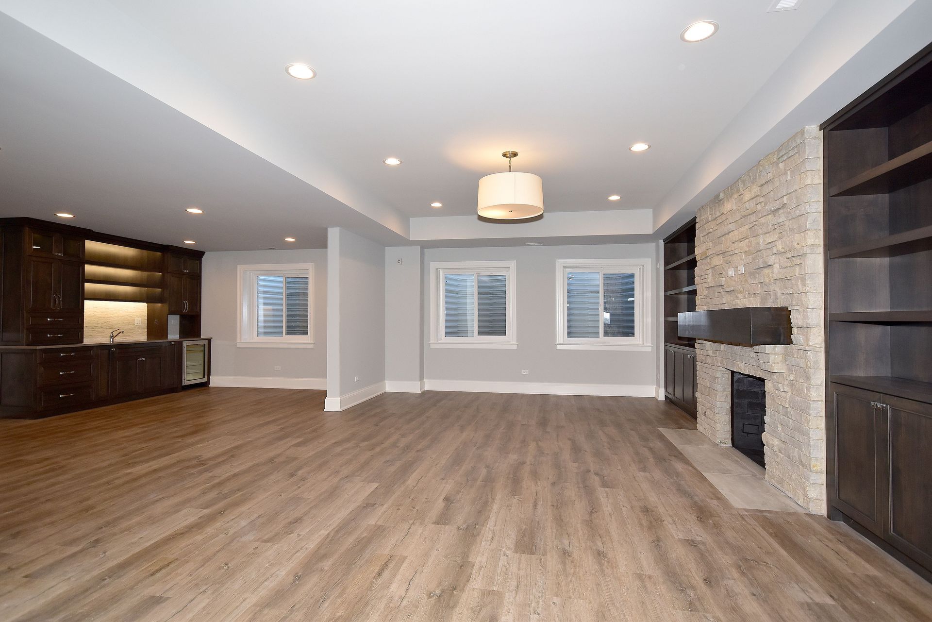 Spacious modern living room with wood floors, recessed lights, windows, and a stone fireplace mantel