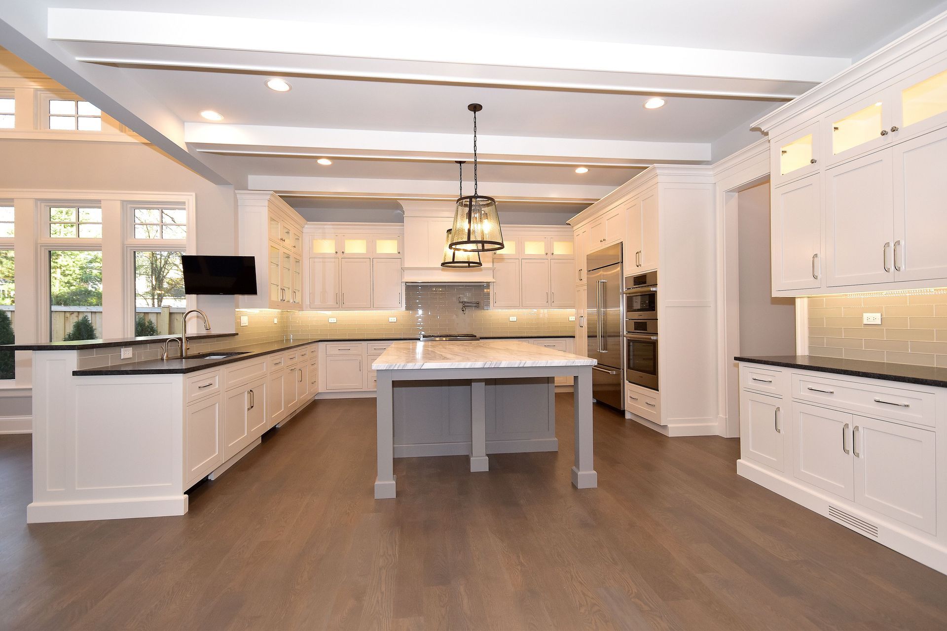 Bright modern kitchen with white cabinets, large island, hardwood floors, and pendant lighting