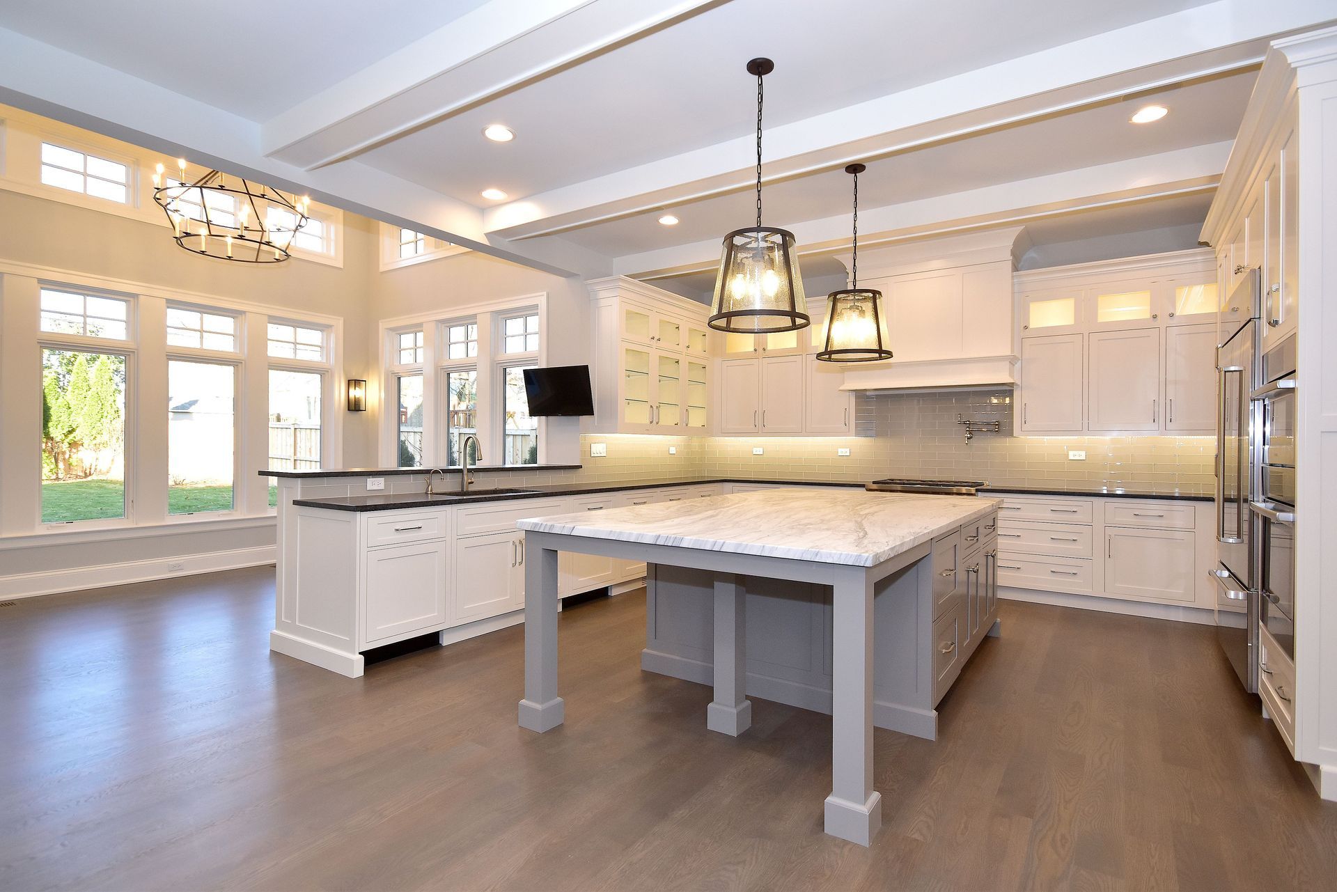 Bright modern kitchen with white cabinets, marble island, pendant lights, and wood floors