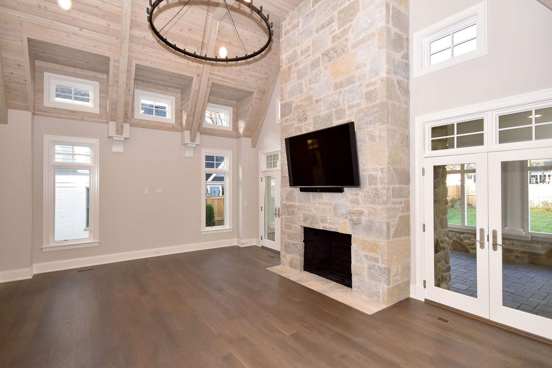 Spacious living room with stone fireplace, mounted TV, high ceiling, and glass French doors.