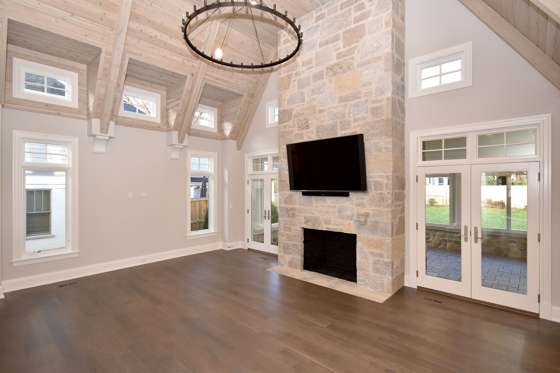 Spacious living room with stone fireplace, dark wood floors, high windows, and French doors to a patio.