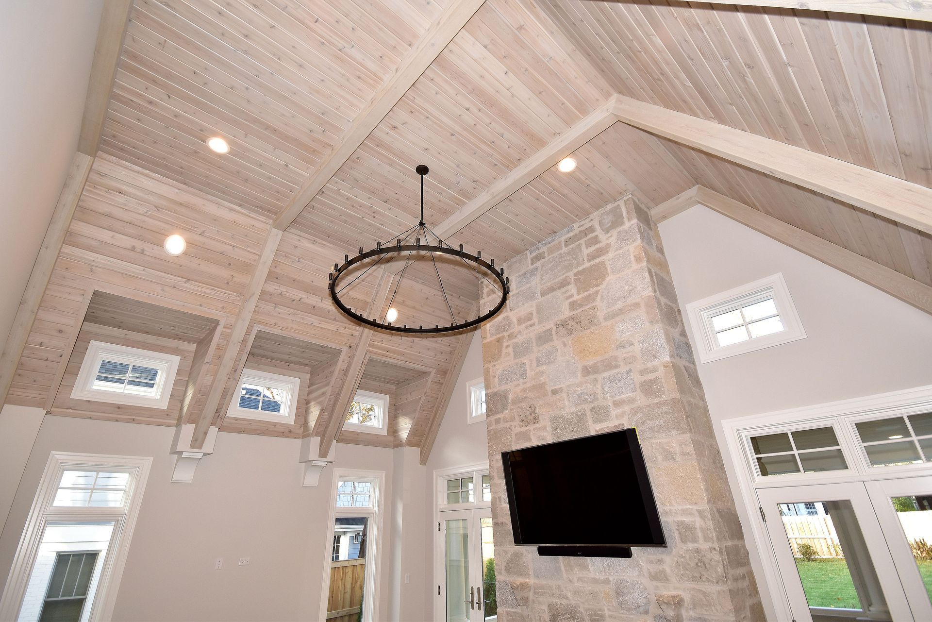 Bright vaulted living room with white wood ceilings, stone fireplace, and hanging chandelier.