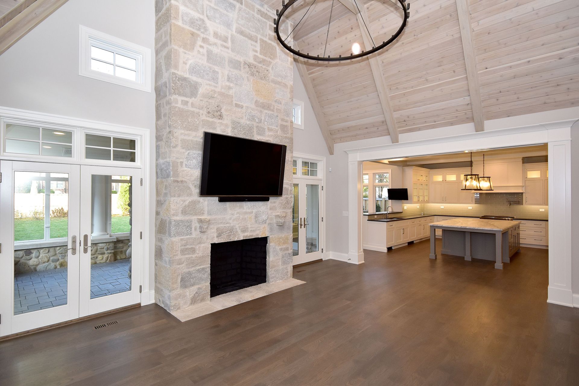 Spacious modern living room with stone fireplace, wall-mounted TV, and open kitchen with island