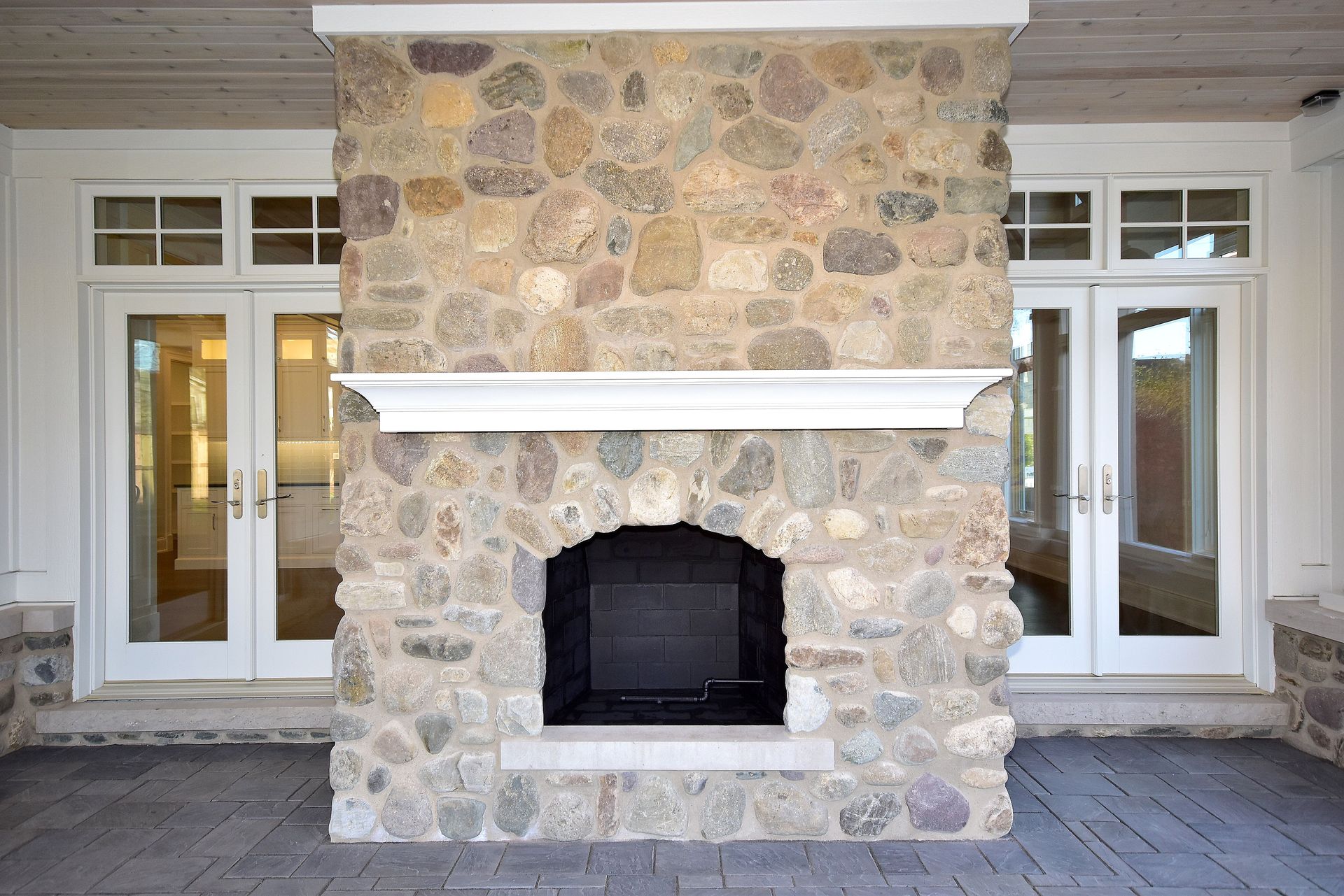 Stone fireplace with white mantel centered between two glass French doors on a covered porch