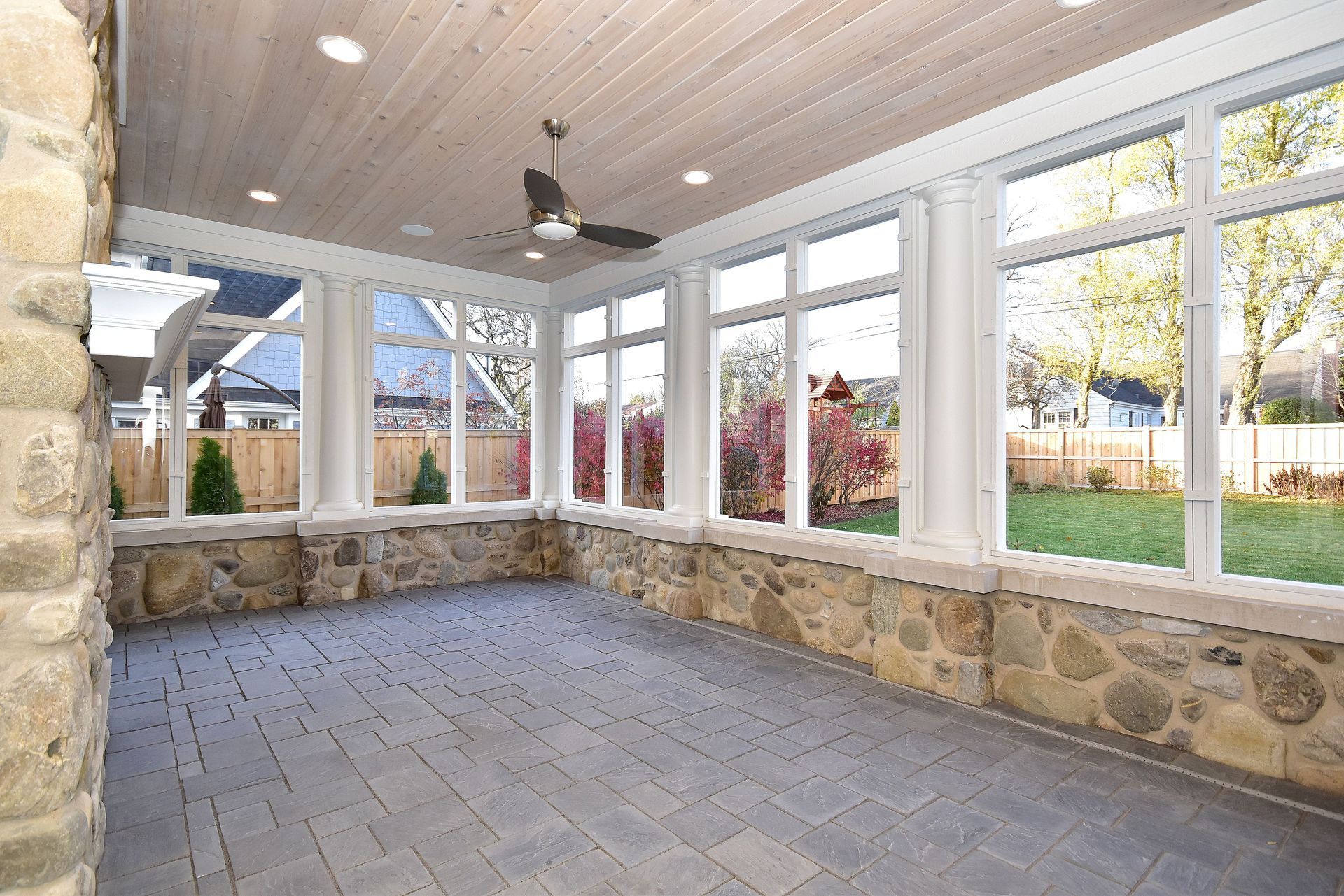 Covered sunroom with stone walls, gray tile floor, white windows, and ceiling fan overlooking a yard