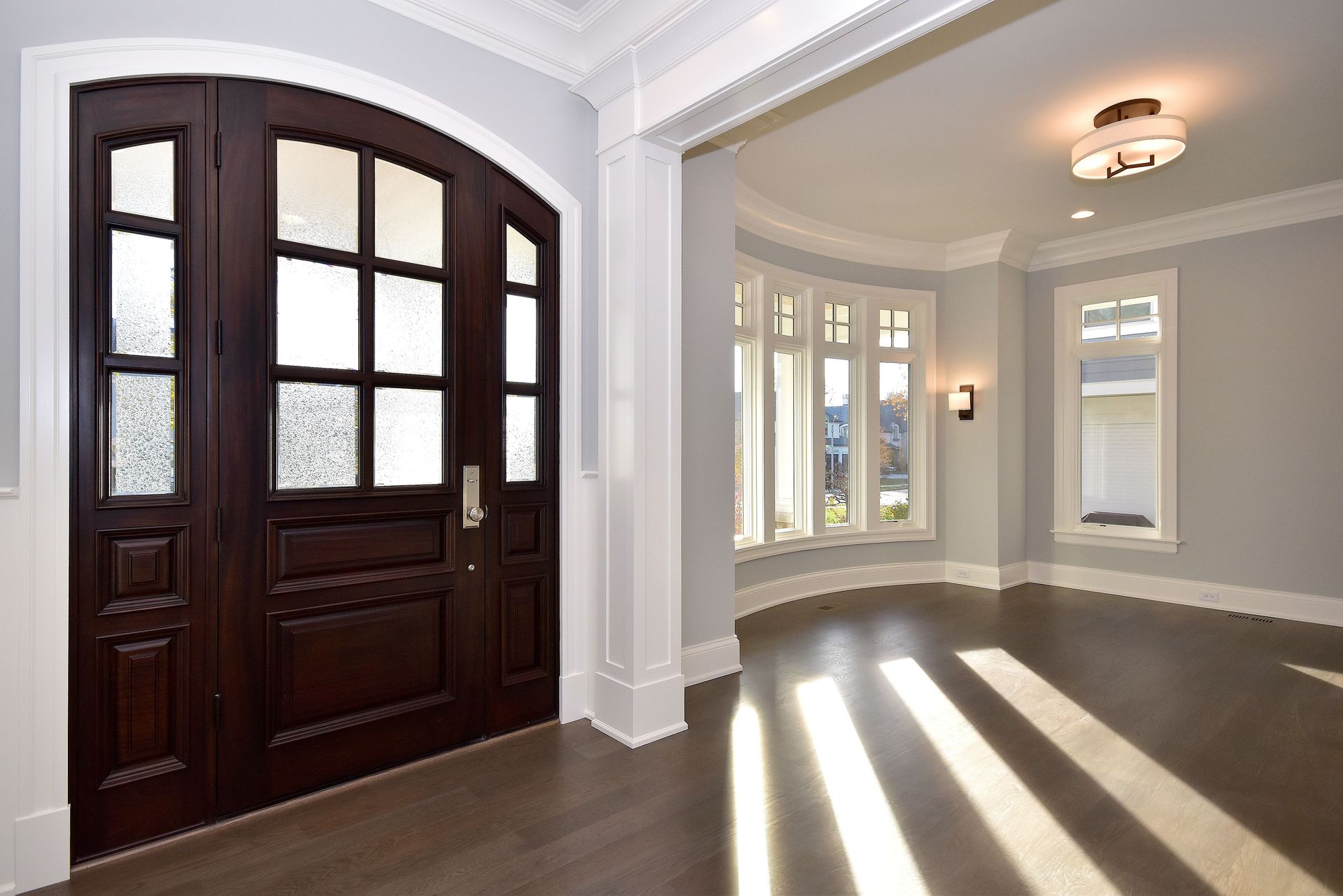 Interior entryway with dark wood double doors, arched opening, and sunlight streaming across hardwood floors