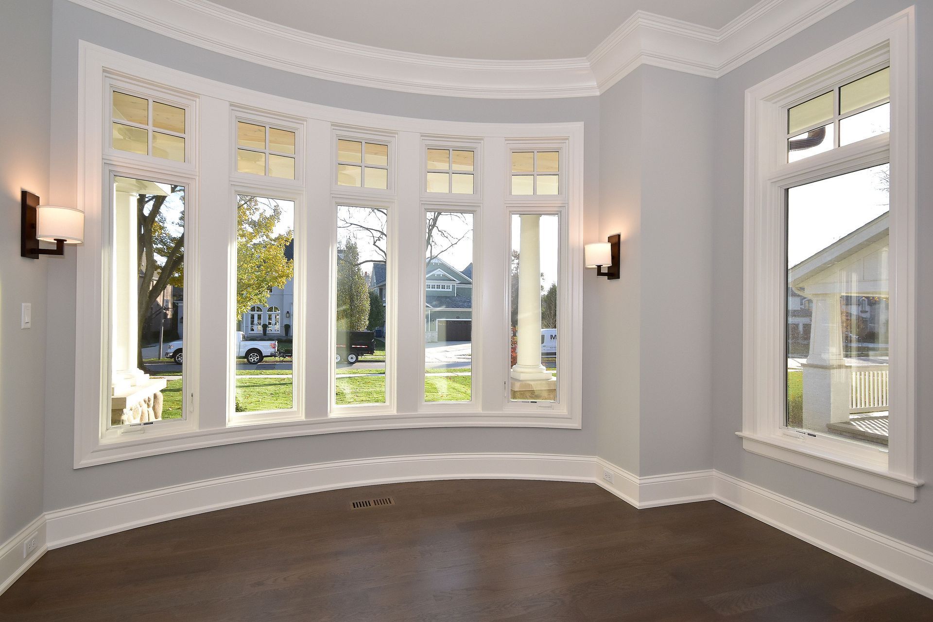 Empty bright bay window room with white trim, gray walls, and dark wood floors