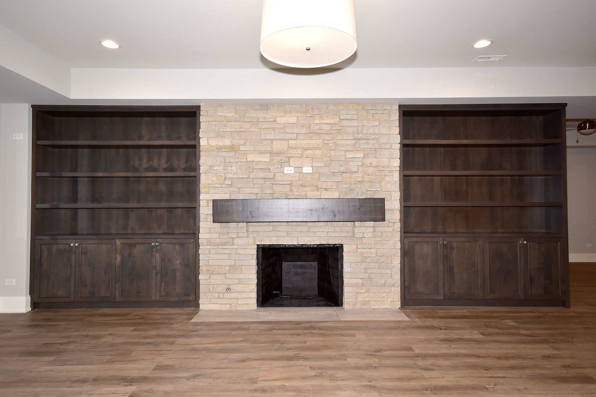 Living room wall with two dark built-in shelves, a stone fireplace, and wood flooring