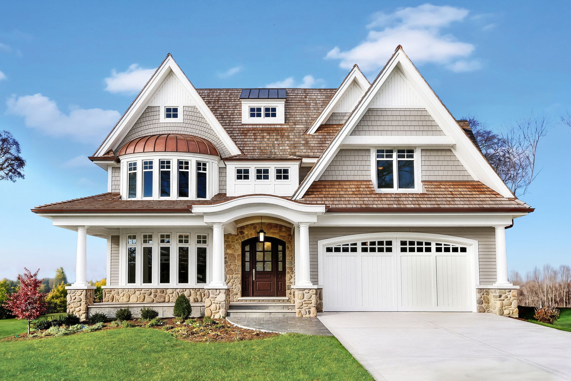Large modern suburban house with stone accents, white trim, and a two-car garage under a blue sky