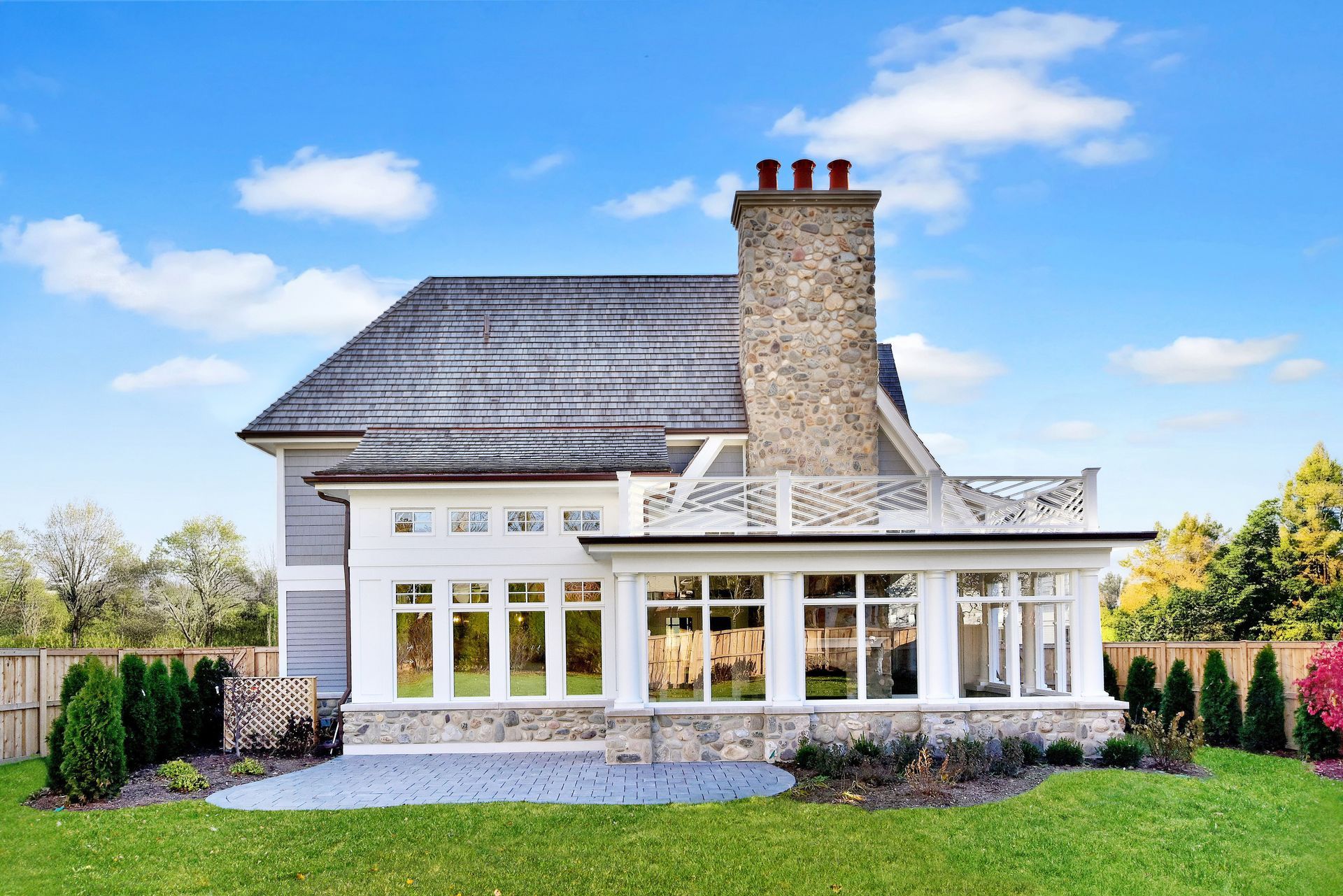 White house with a stone chimney and large windows, set on a green lawn under a blue sky.