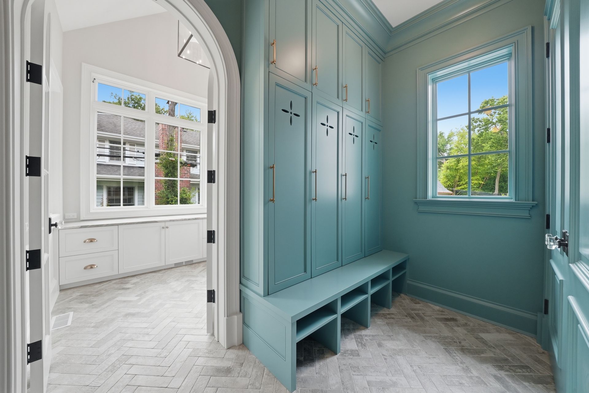 Blue entryway with built-in bench and hooks, opening to a bright white room through an arched doorway