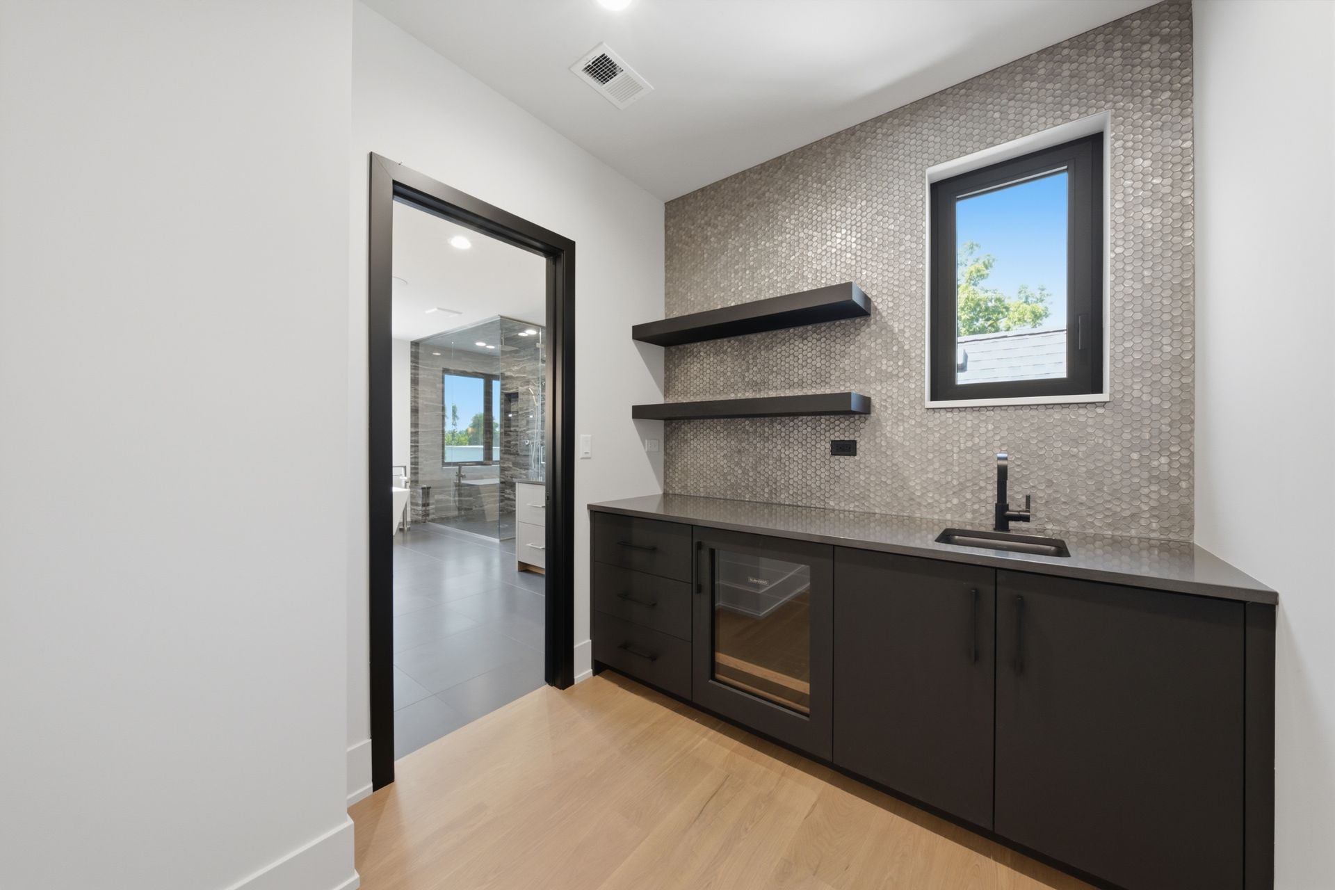 Modern kitchenette with dark cabinets, black shelves, sink, and a small window in a bright room