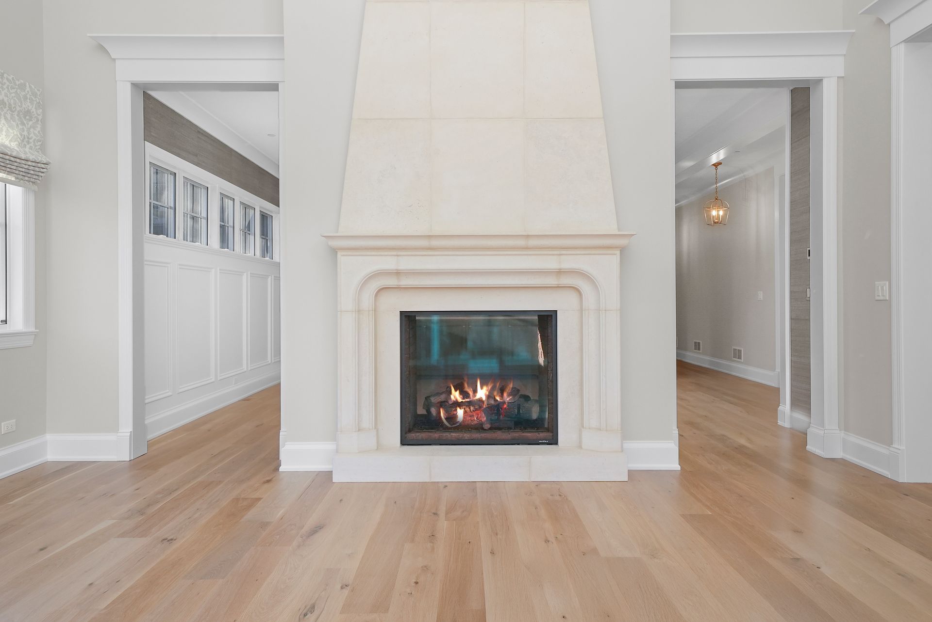 Bright living room with a white fireplace, hardwood floors, and open doorways on both sides.