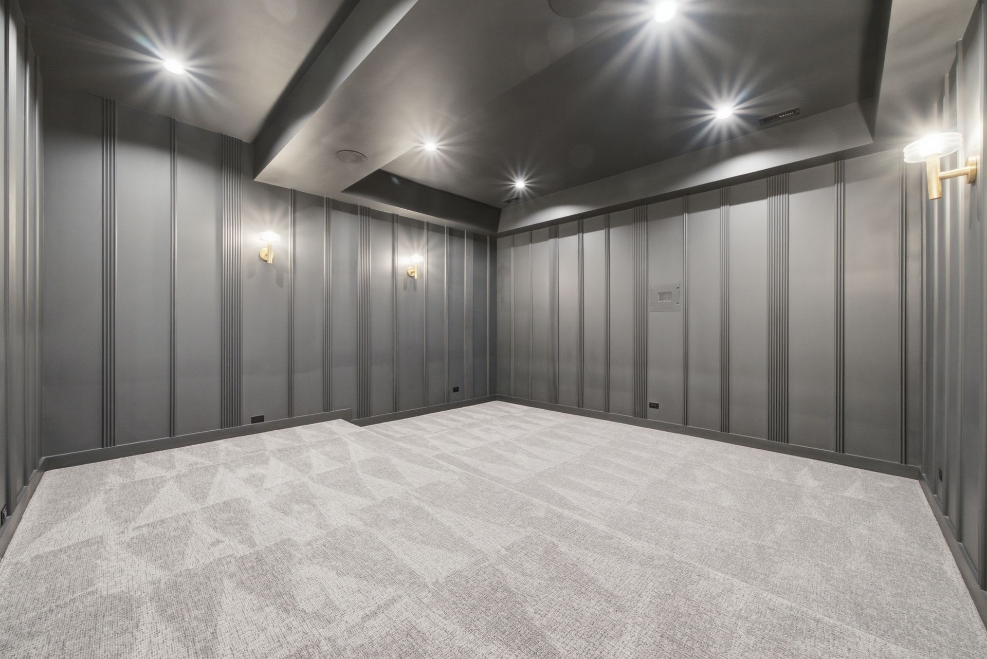 Empty modern room with gray paneled walls, recessed ceiling lights, and light carpet flooring.