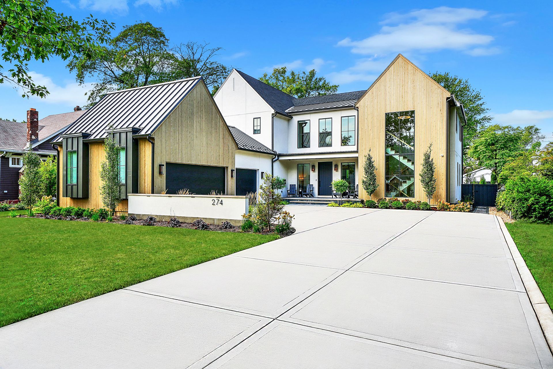 Modern house with wood accents, green lawn, and a wide concrete driveway under a blue sky