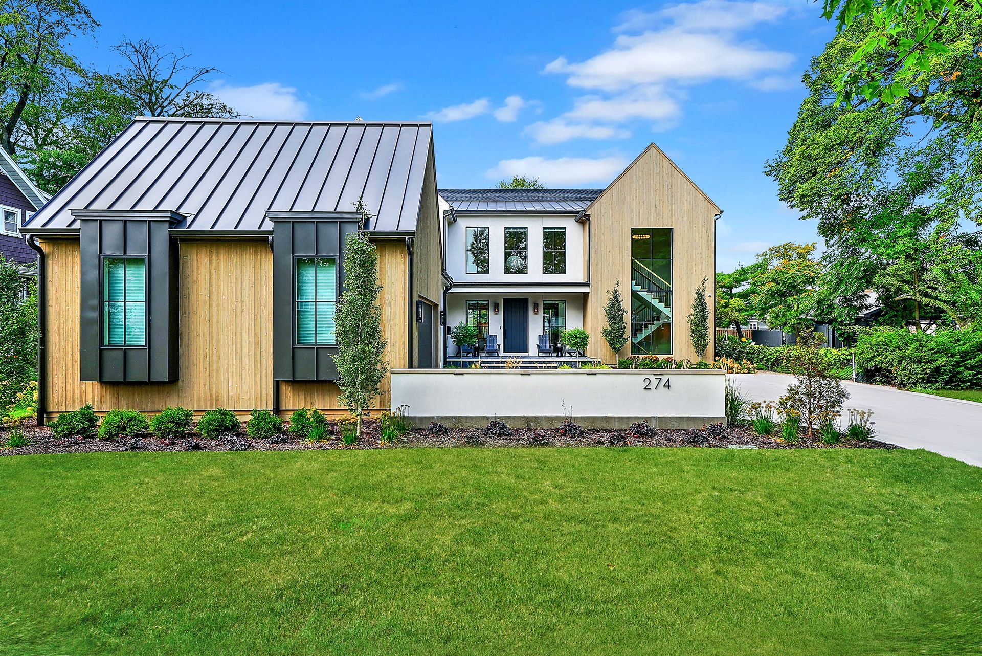Modern house with wood and white facade, metal roof, and large green lawn under a blue sky