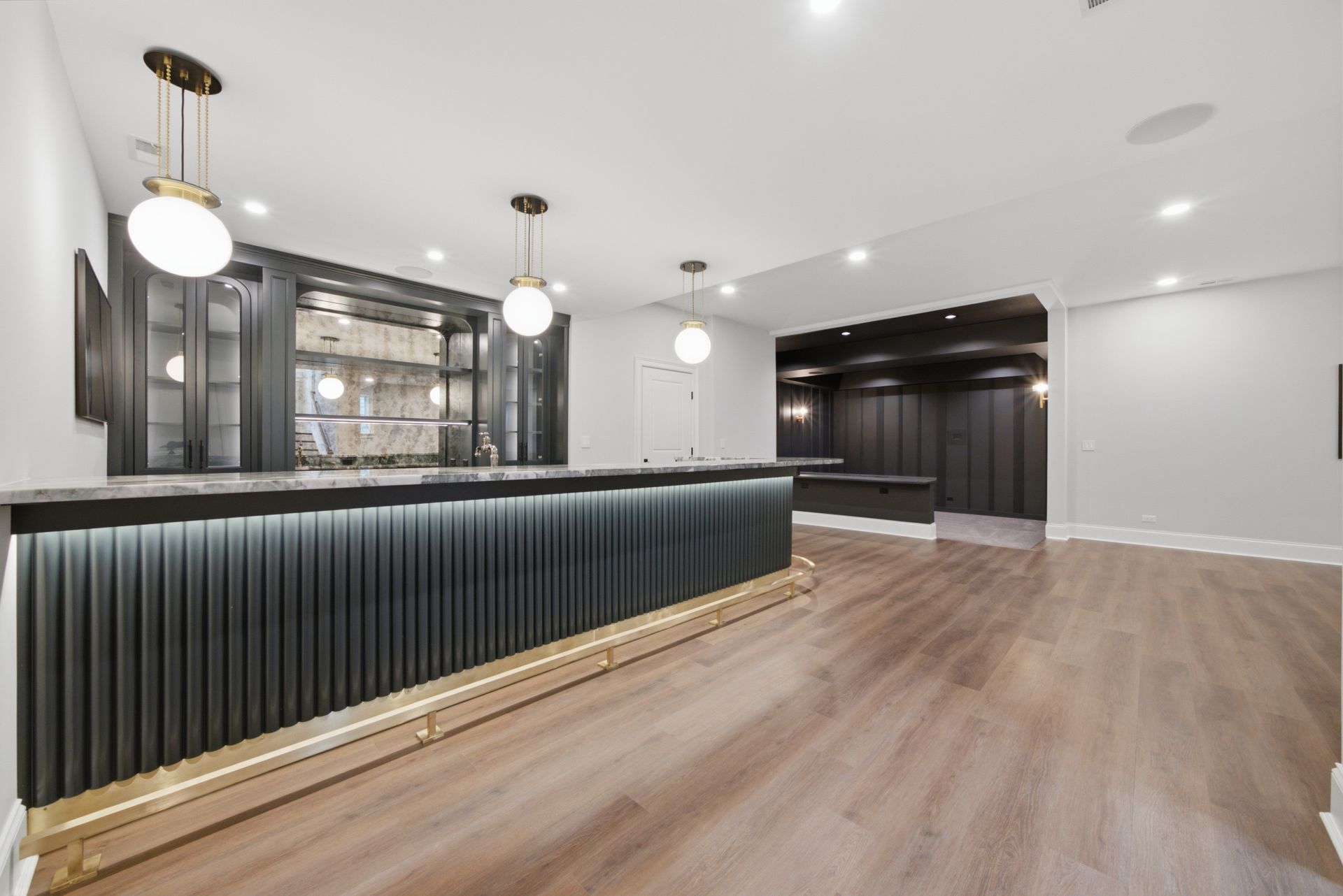 Modern empty home bar with dark cabinetry, pendant lights, and light wood flooring