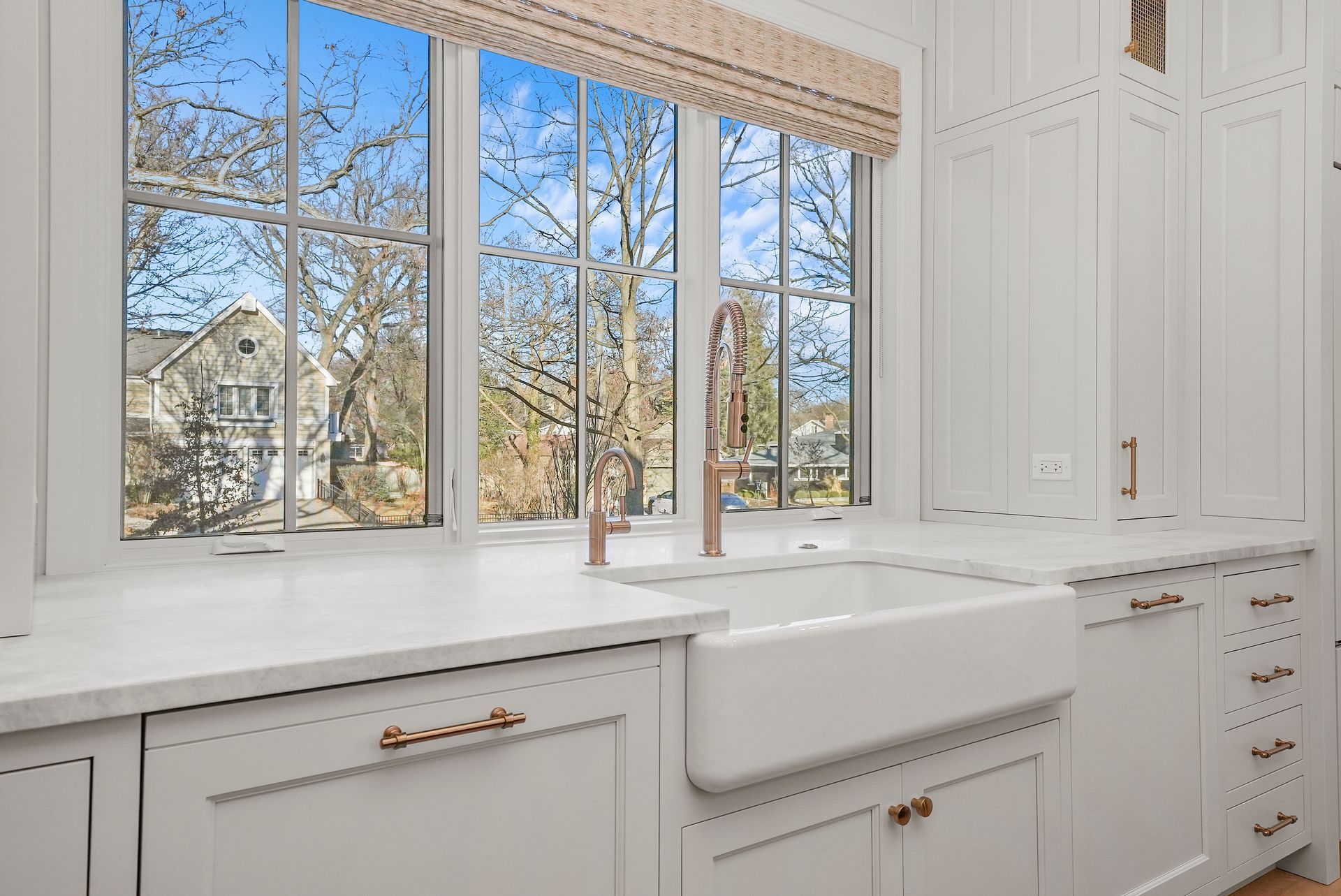 Bright white kitchen sink beneath large windows with a view of trees outside
