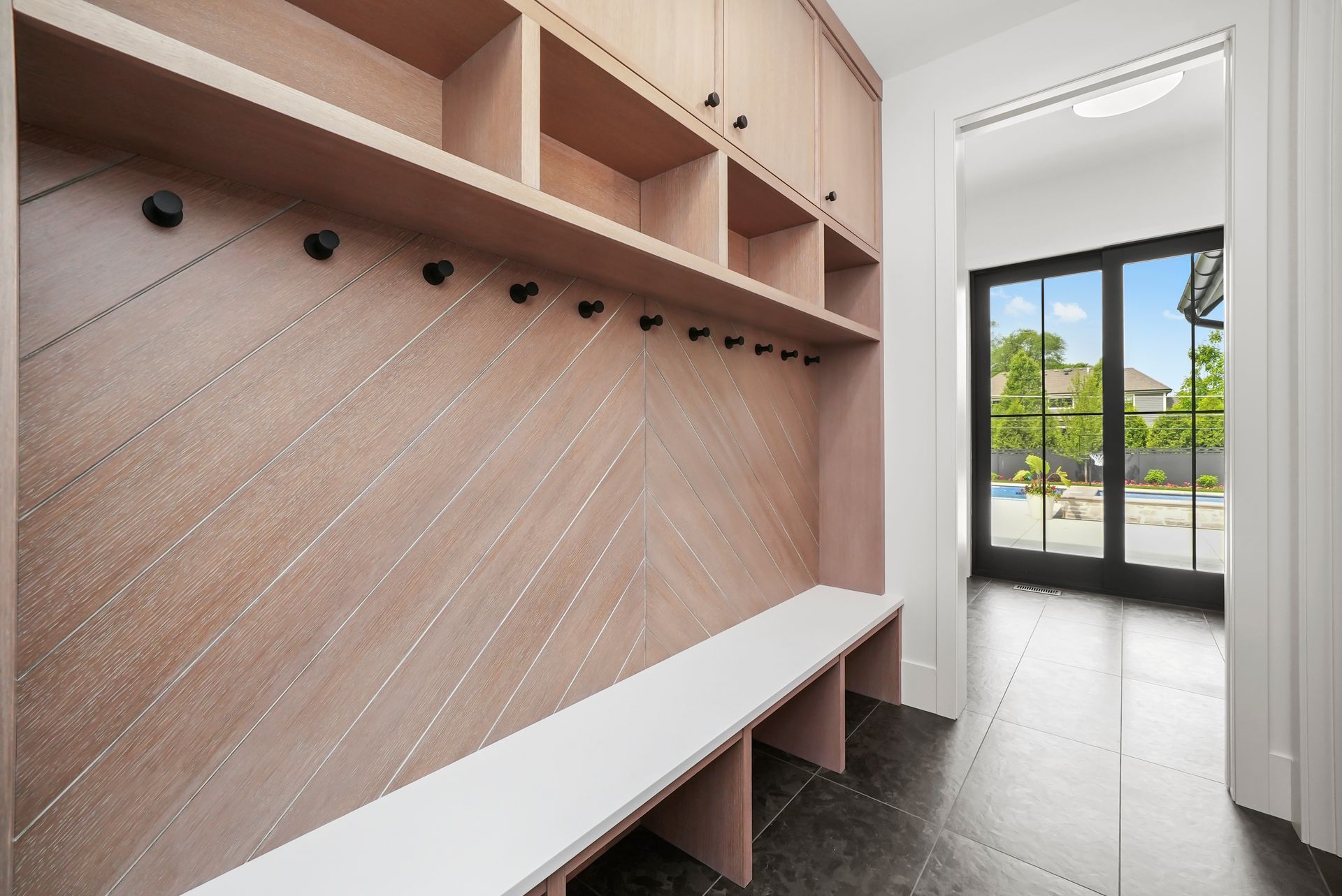 Modern mudroom with pink built-in bench, coat hooks, cubbies, and glass door to patio.