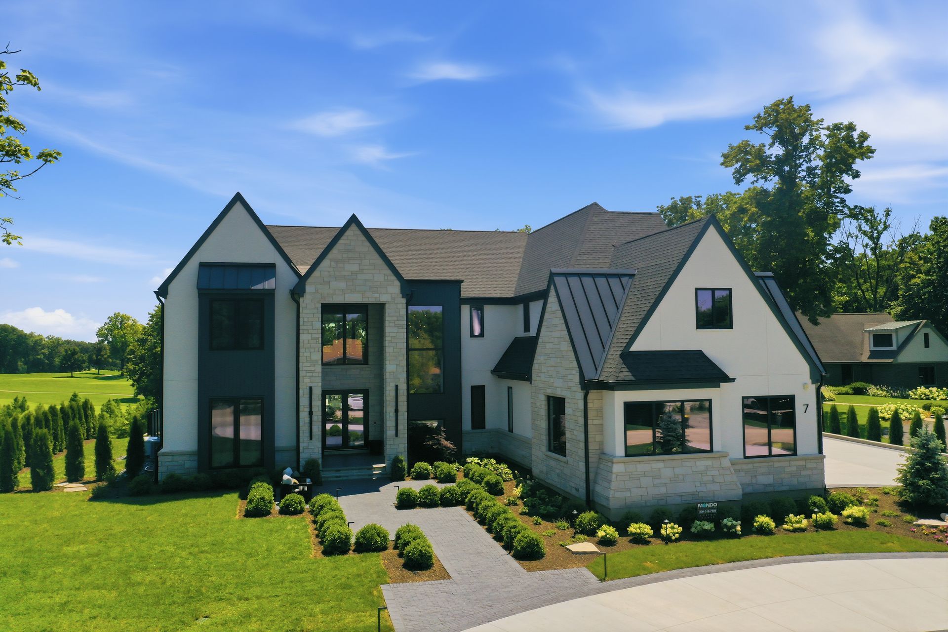 Modern two-story house with gray roof, white exterior, and landscaped front lawn under a blue sky