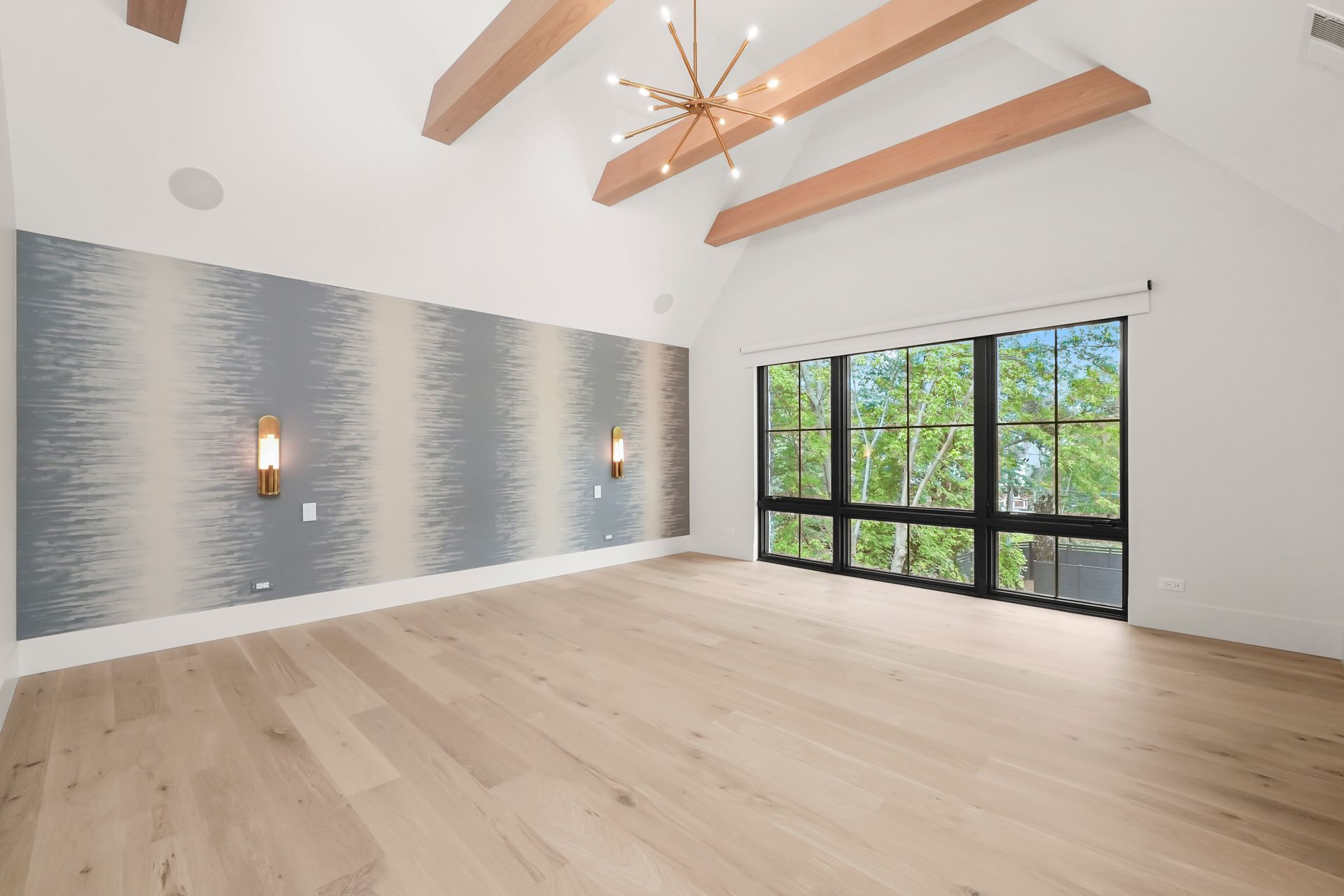 Spacious modern living room with light wood floors, wood ceiling beams, and large windows overlooking greenery