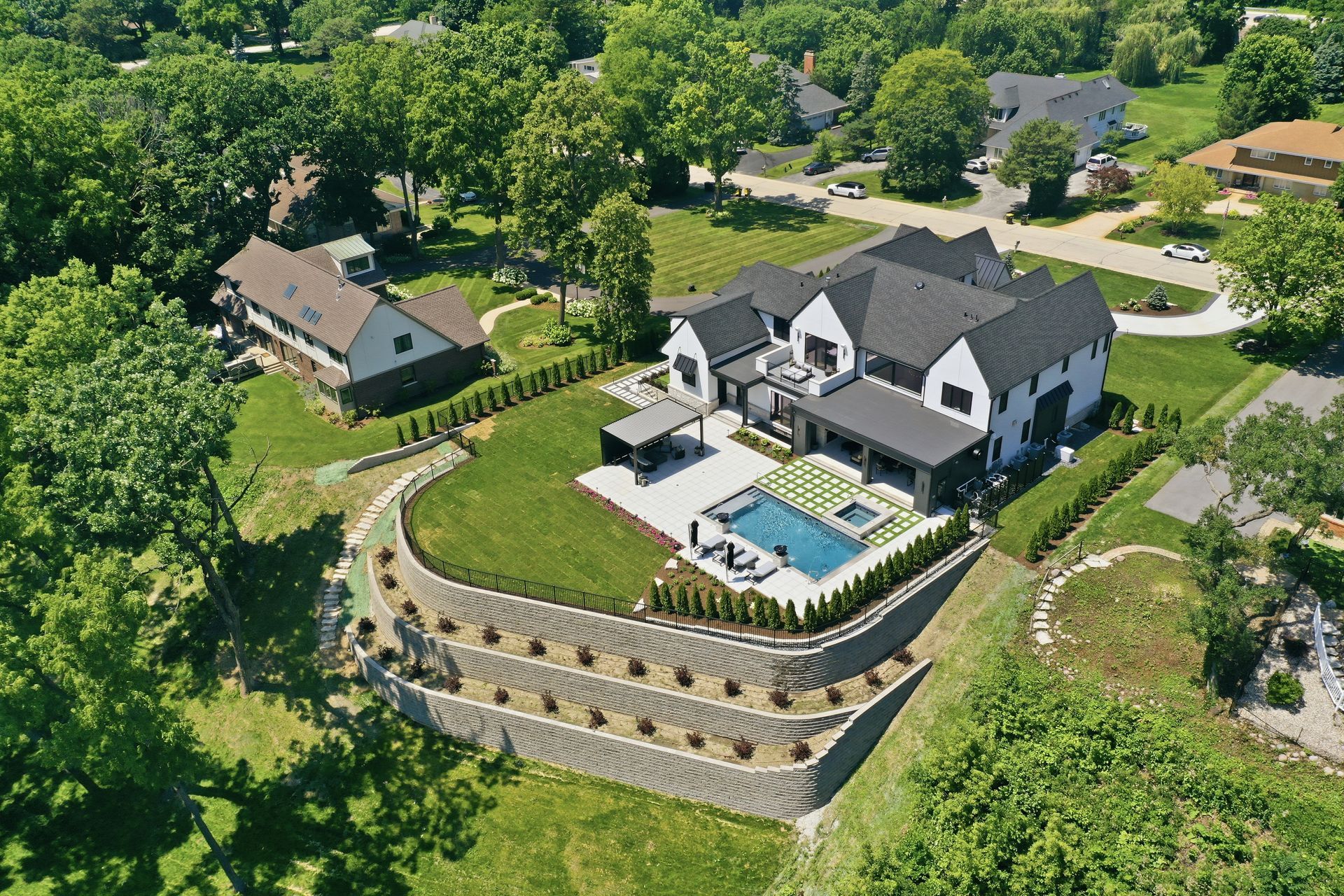 Aerial view of a large modern house with a backyard pool, patio, and landscaped hillside surrounded by trees